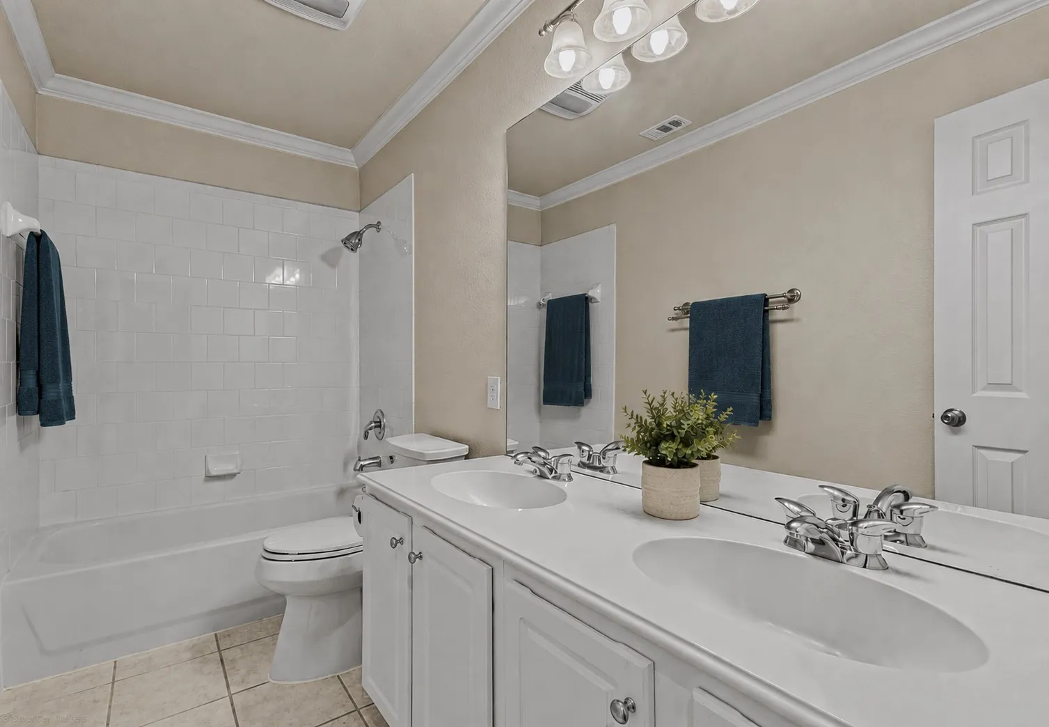 Dual vanity with integrated sinks, white cabinetry, chrome fixtures, and a shower-over-tub combination with subway tile surround