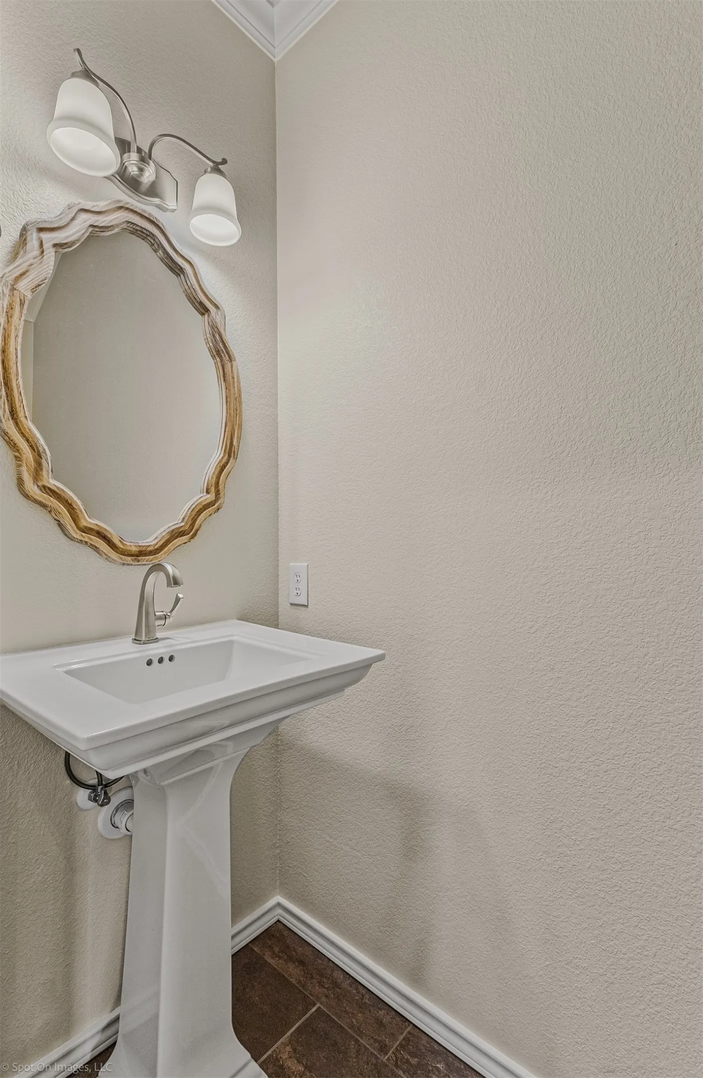 Pedestal sink with a polished chrome faucet, decorative oval mirror, and a two-light vanity fixture