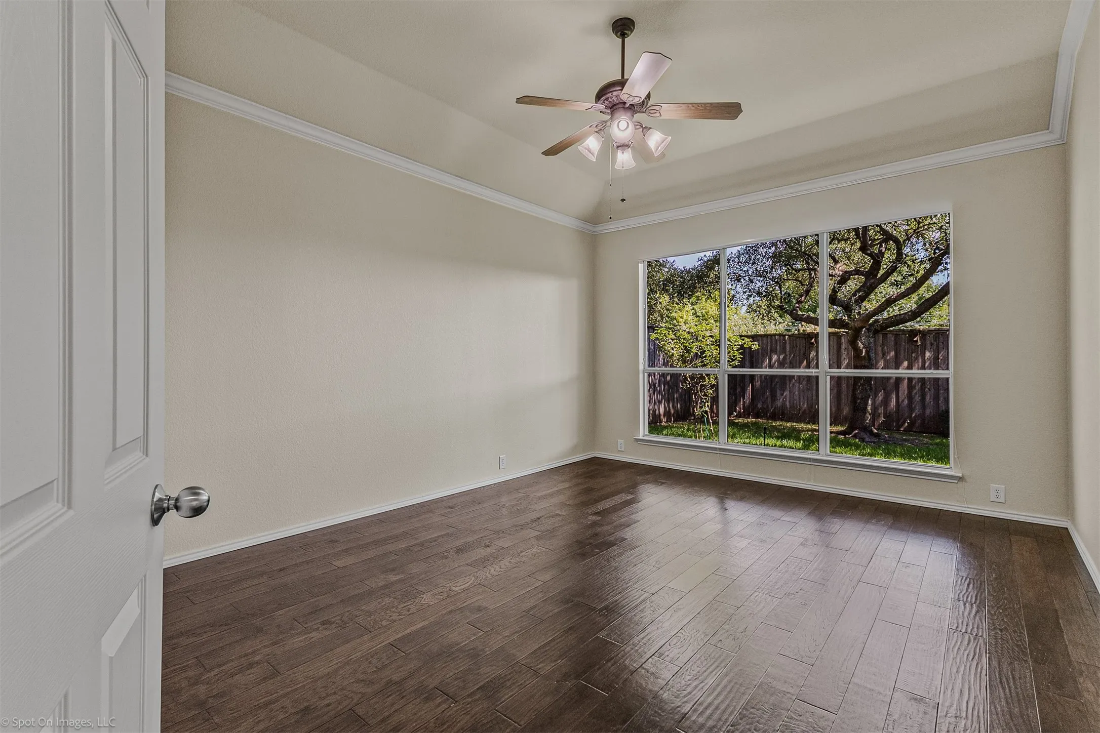 Vaulted ceiling with crown molding, ceiling fan with light fixture, wood-finish flooring, and a large multi-pane window