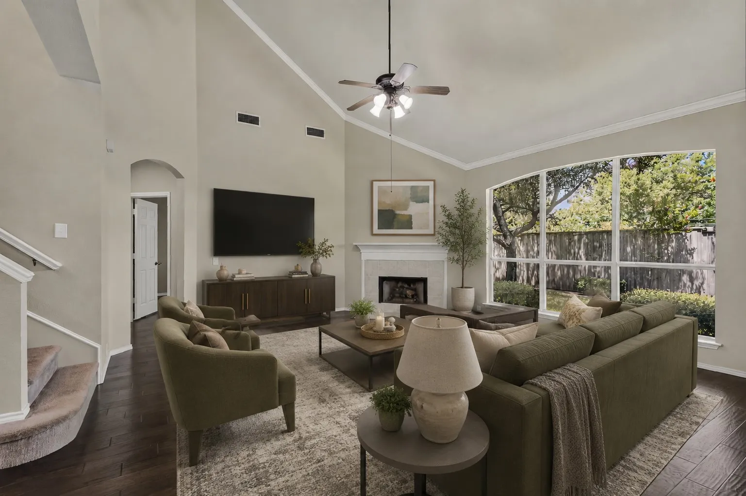 Vaulted ceiling with crown molding, a fireplace with a mantel, and a large arched window