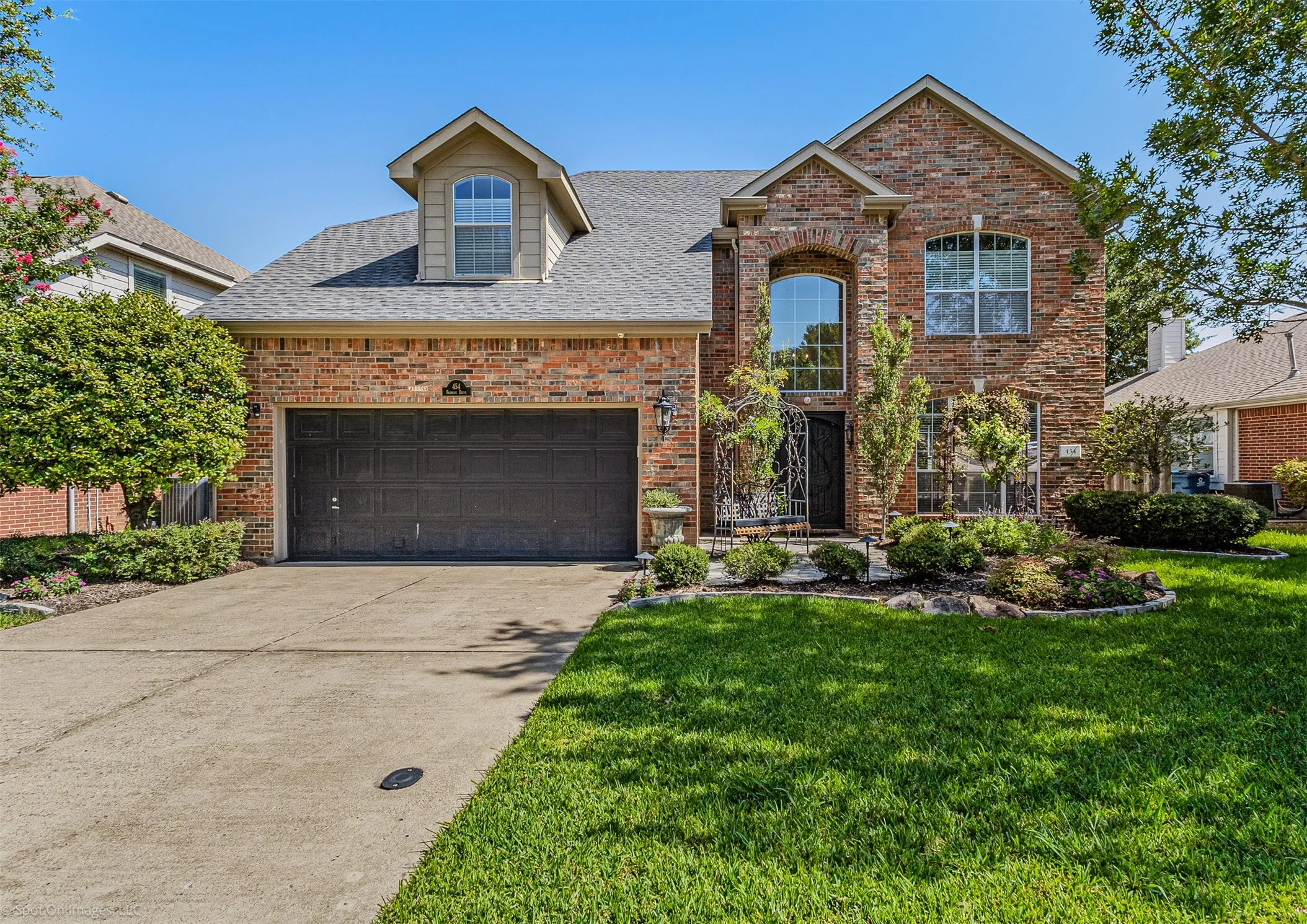 Brick exterior, two-car garage, dormer window, established landscaping, and a manicured lawn