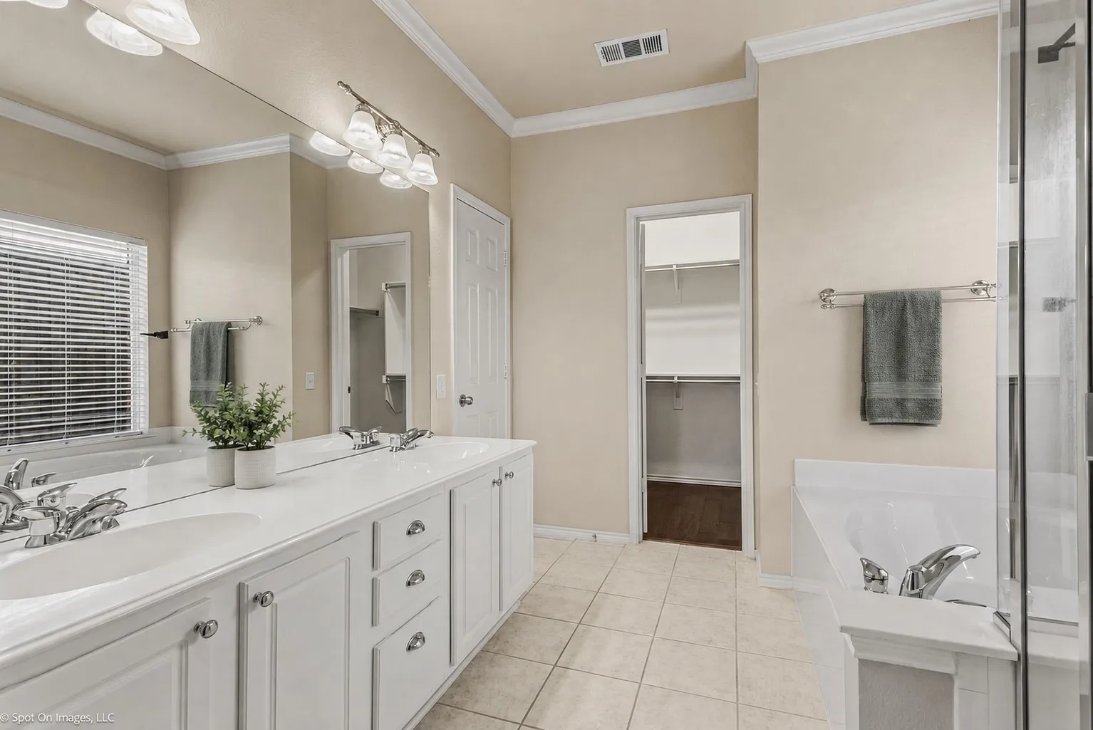 Dual vanity with white cabinetry, tile flooring, built-in bathtub, and an adjacent walk-in closet