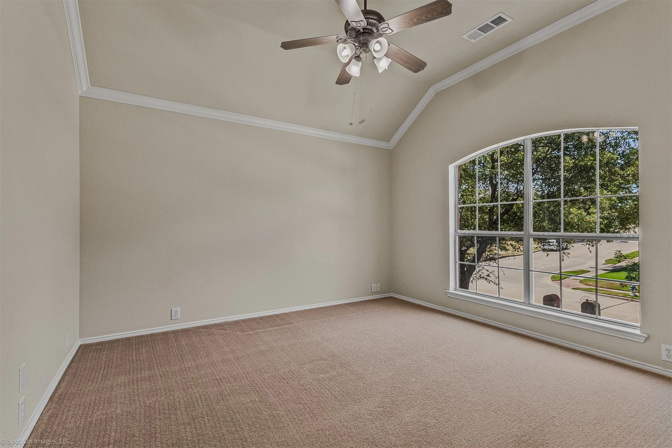 Vaulted ceiling with crown molding, arched window, ceiling fan with light fixture, and carpet flooring
