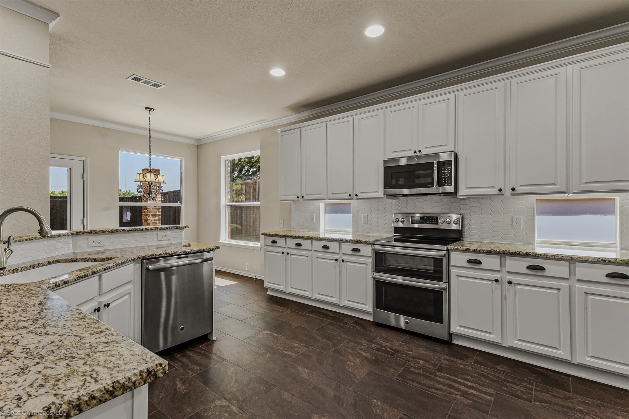 Well-appointed kitchen featuring granite countertops, extensive white cabinetry, stainless steel appliances, a tile backsplash, and dark wood-finish flooring