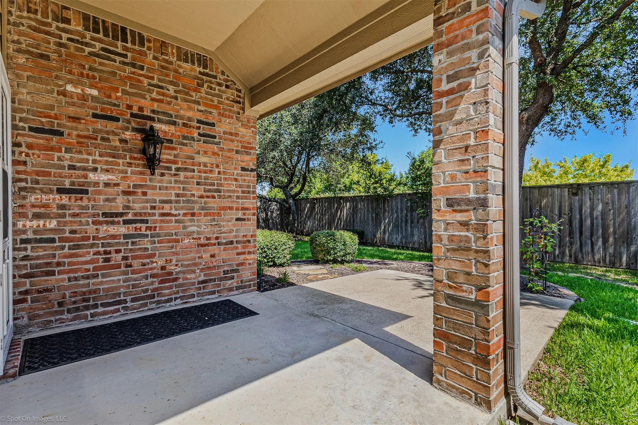 Covered patio featuring a brick exterior, concrete flooring, and a decorative wall-mounted light fixture