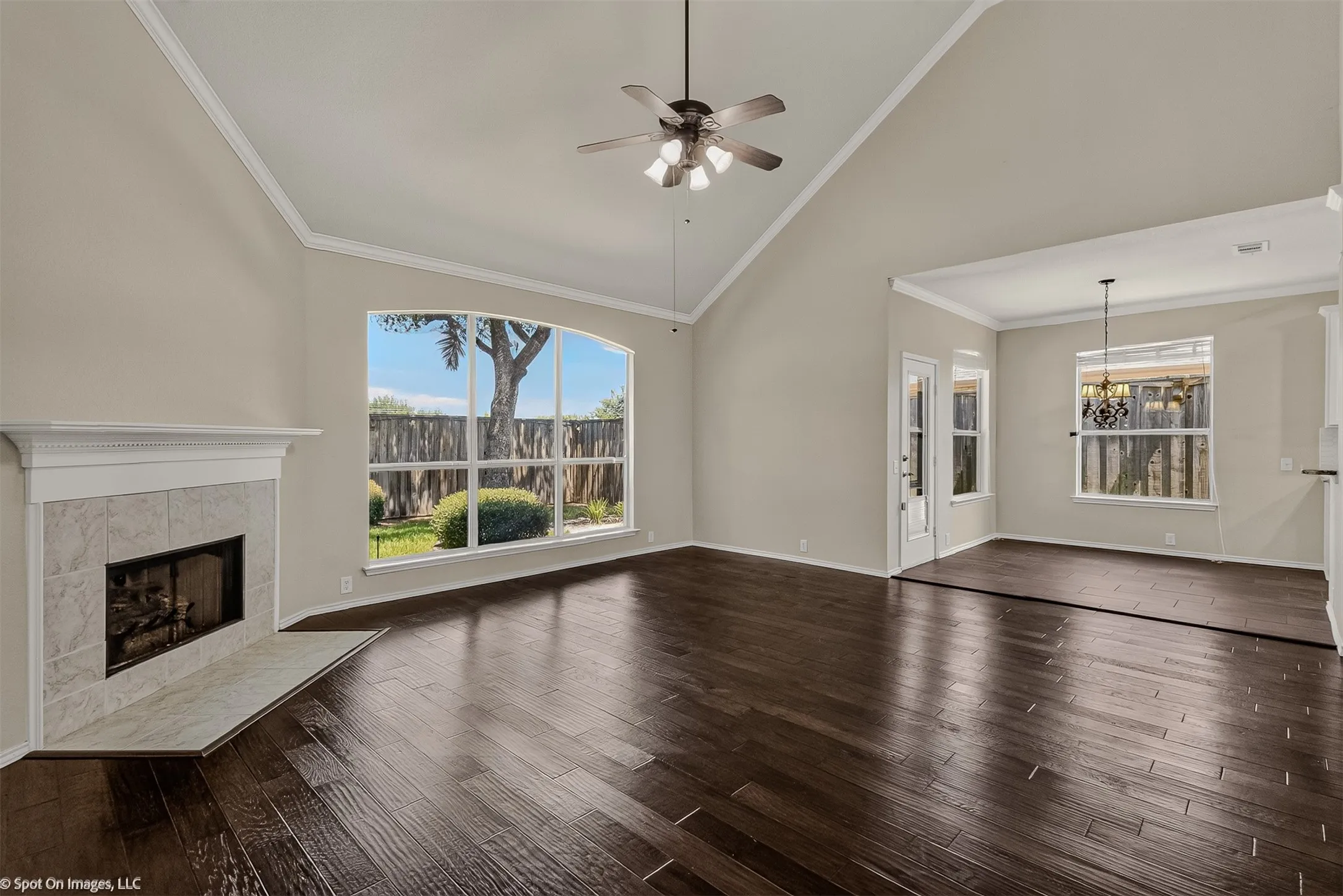 Vaulted ceiling with a ceiling fan, wood-finish flooring, tiled fireplace, and an arched window