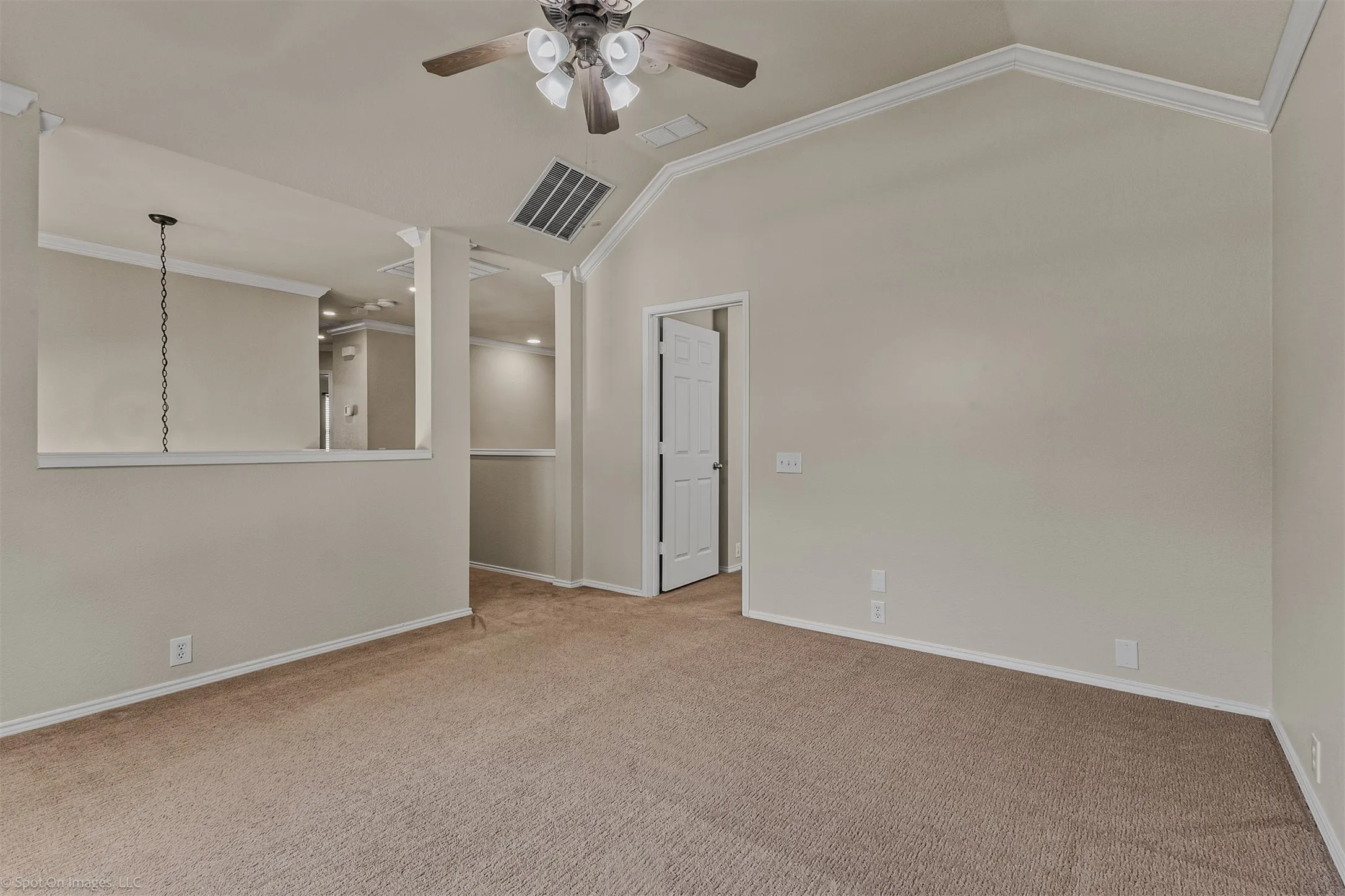 Vaulted ceiling with crown molding, ceiling fan with integrated lighting, carpeted flooring, and a half-wall partition