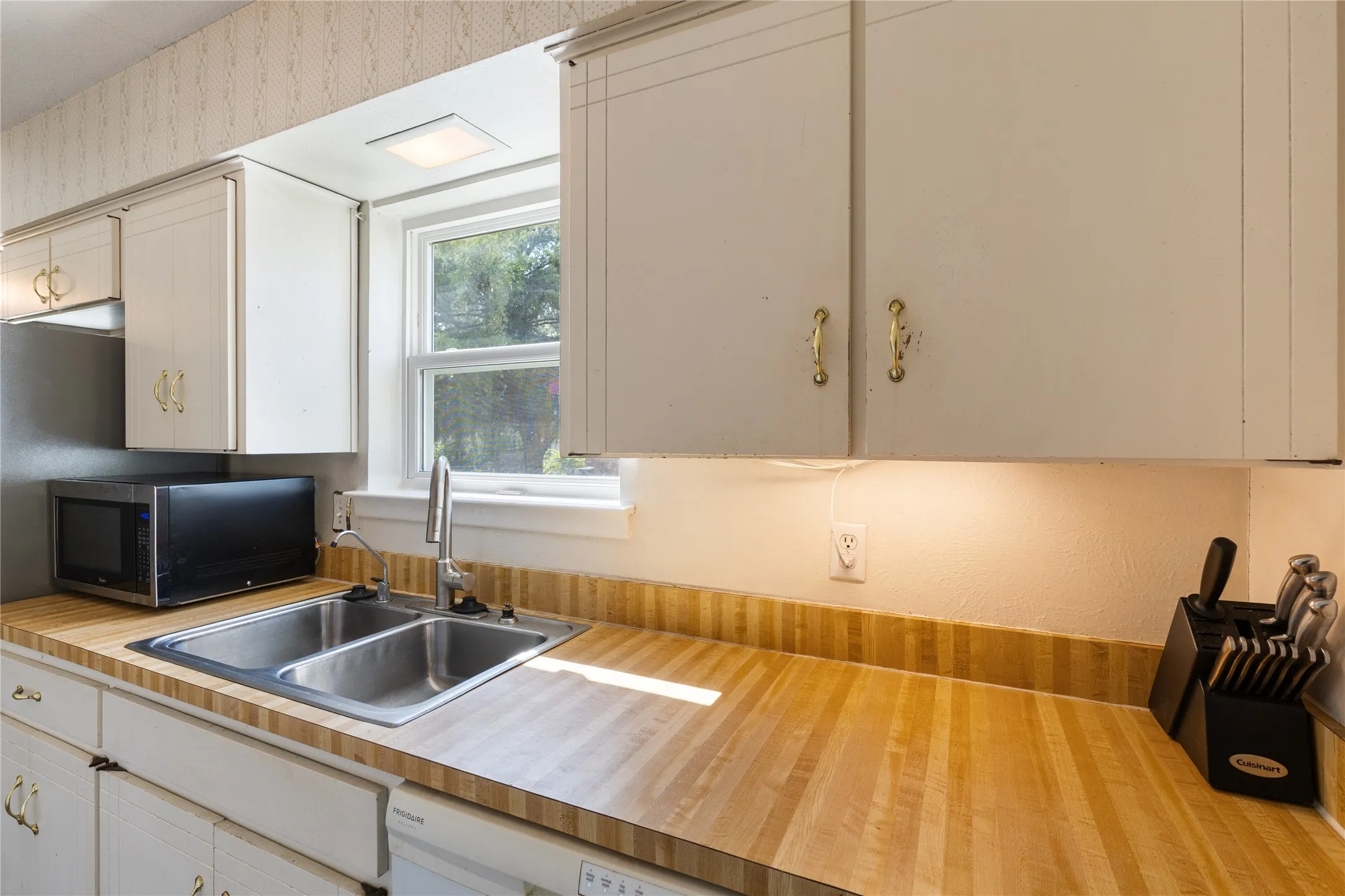 Kitchen featuring light wood-finish countertops, white cabinetry with brass-tone hardware, a double basin stainless steel sink with a gooseneck faucet, and an overhead square light fixture