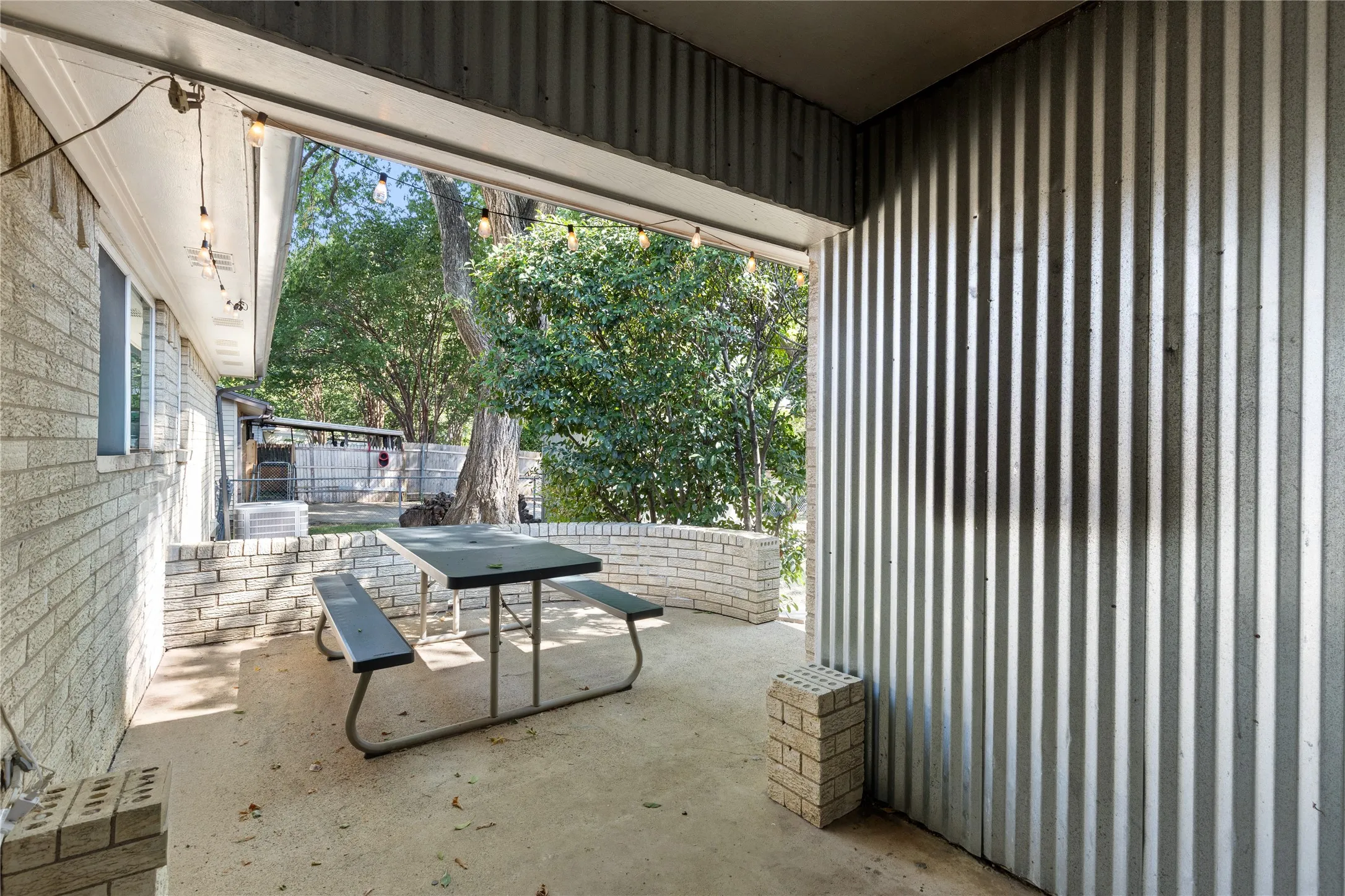 Covered patio featuring a concrete slab, corrugated metal siding, and a light-colored brick half-wall