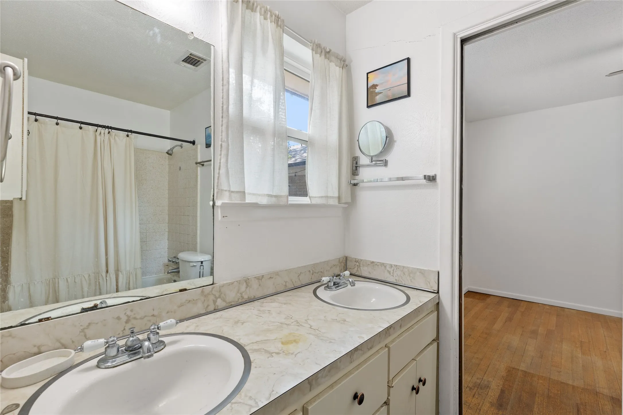 Dual basin vanity with a light-toned countertop, framed mirror, and a window