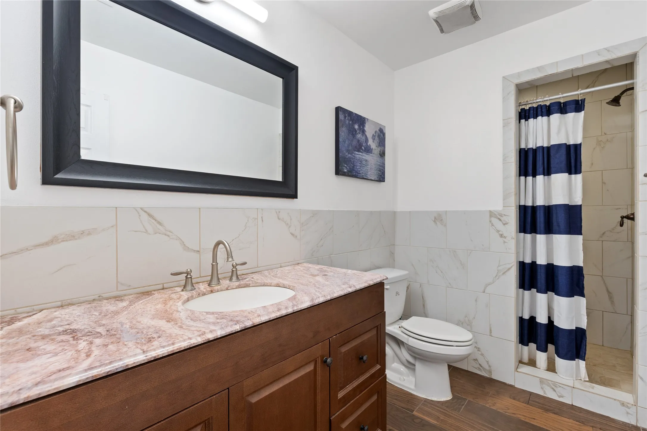 Wood-finish flooring, vanity with integrated sink, and a tiled shower with a dark bronze showerhead