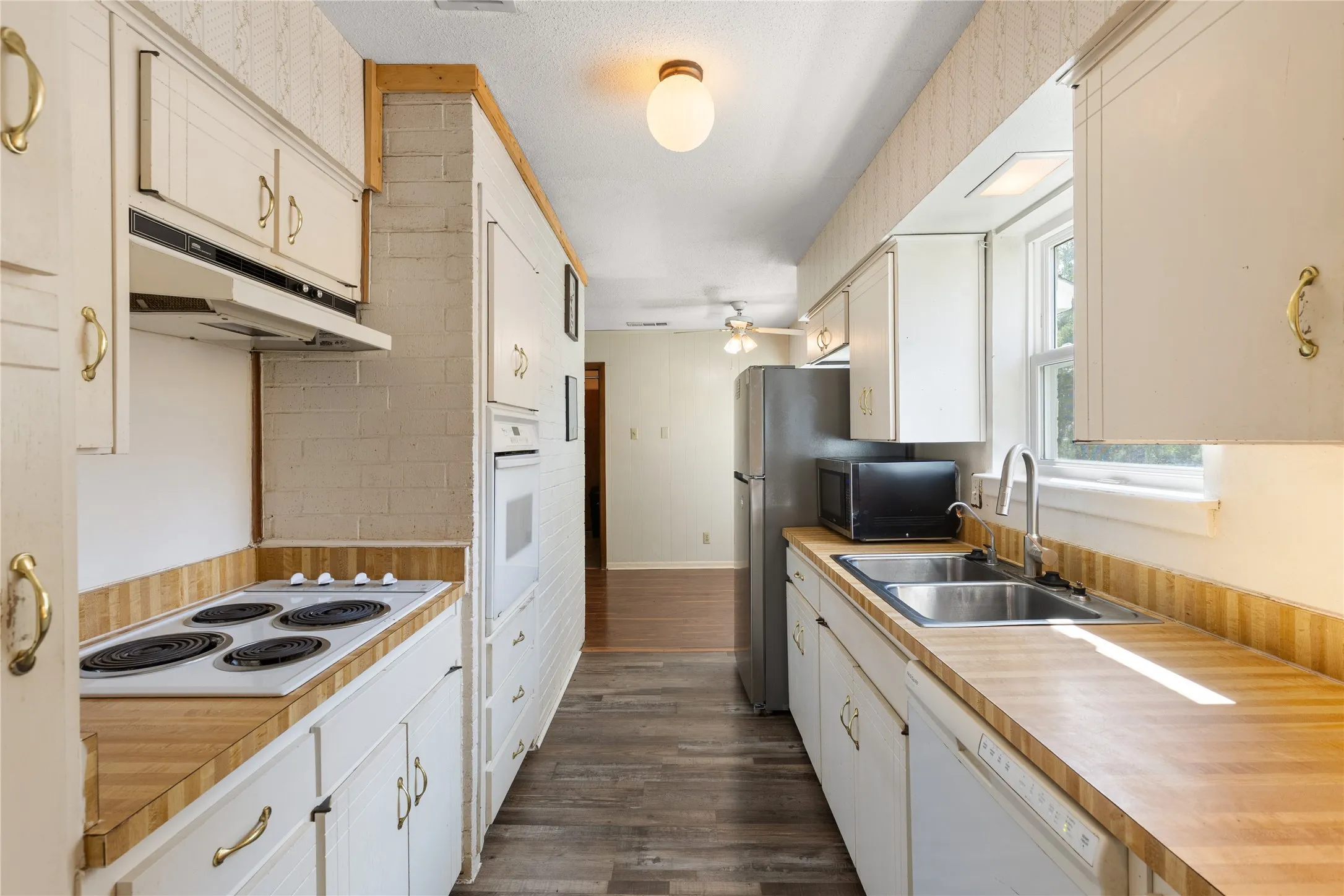 Galley kitchen featuring wood-finish countertops, white cabinetry with brass-tone hardware, and a double basin stainless steel sink