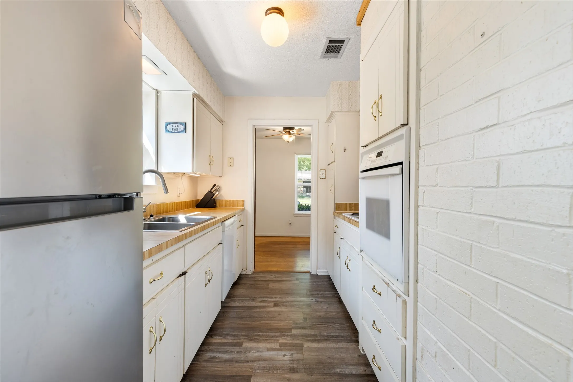 Galley kitchen with wood-finish flooring, light cabinetry, and built-in wall oven