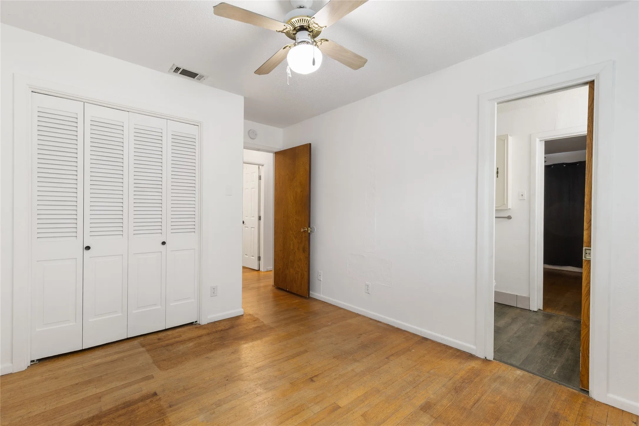Hardwood flooring, ceiling fan with integrated lighting, louvered closet doors, and white painted walls