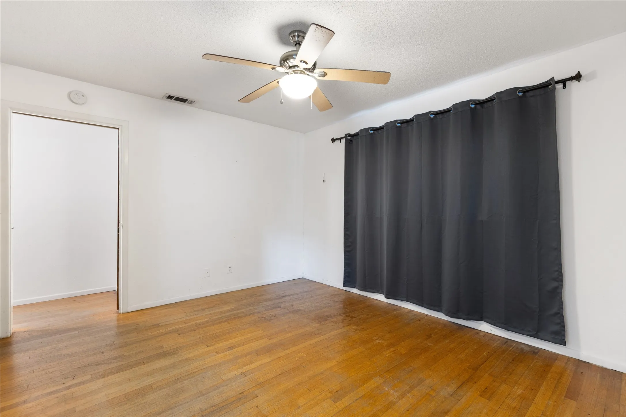 Wood-finish flooring, ceiling fan with integrated lighting, and a doorway opening to another interior space