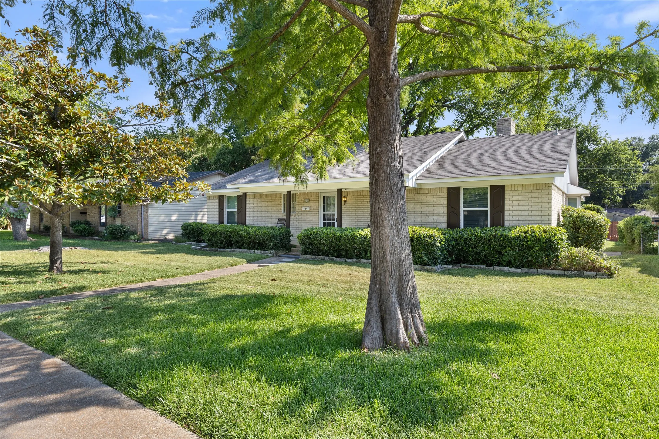 Light-colored brick exterior with dark shutters, gabled roofline, and front porch