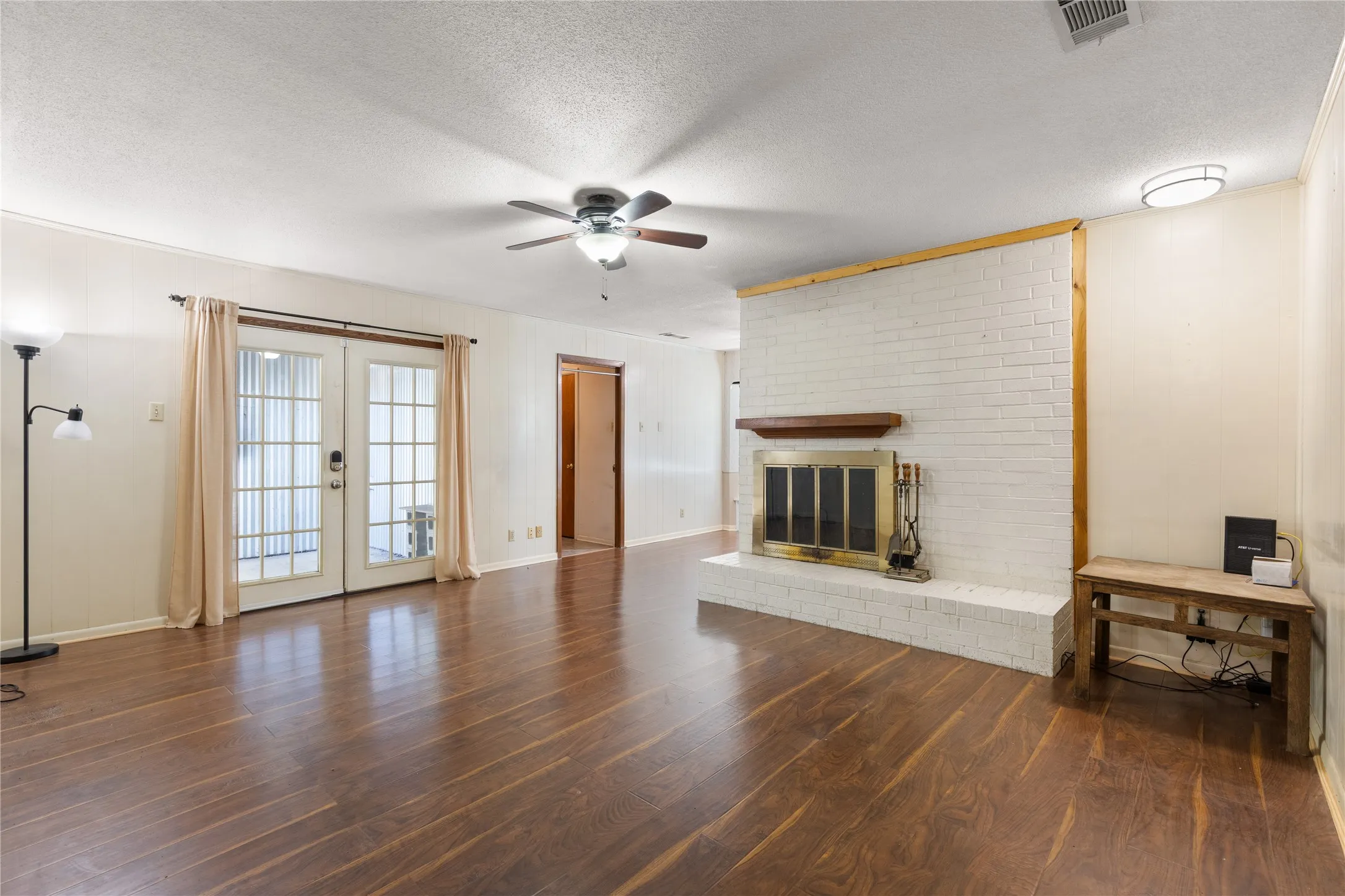 Wood-finish flooring throughout, white painted brick fireplace with wood mantel, French doors, ceiling fan, and recessed lighting