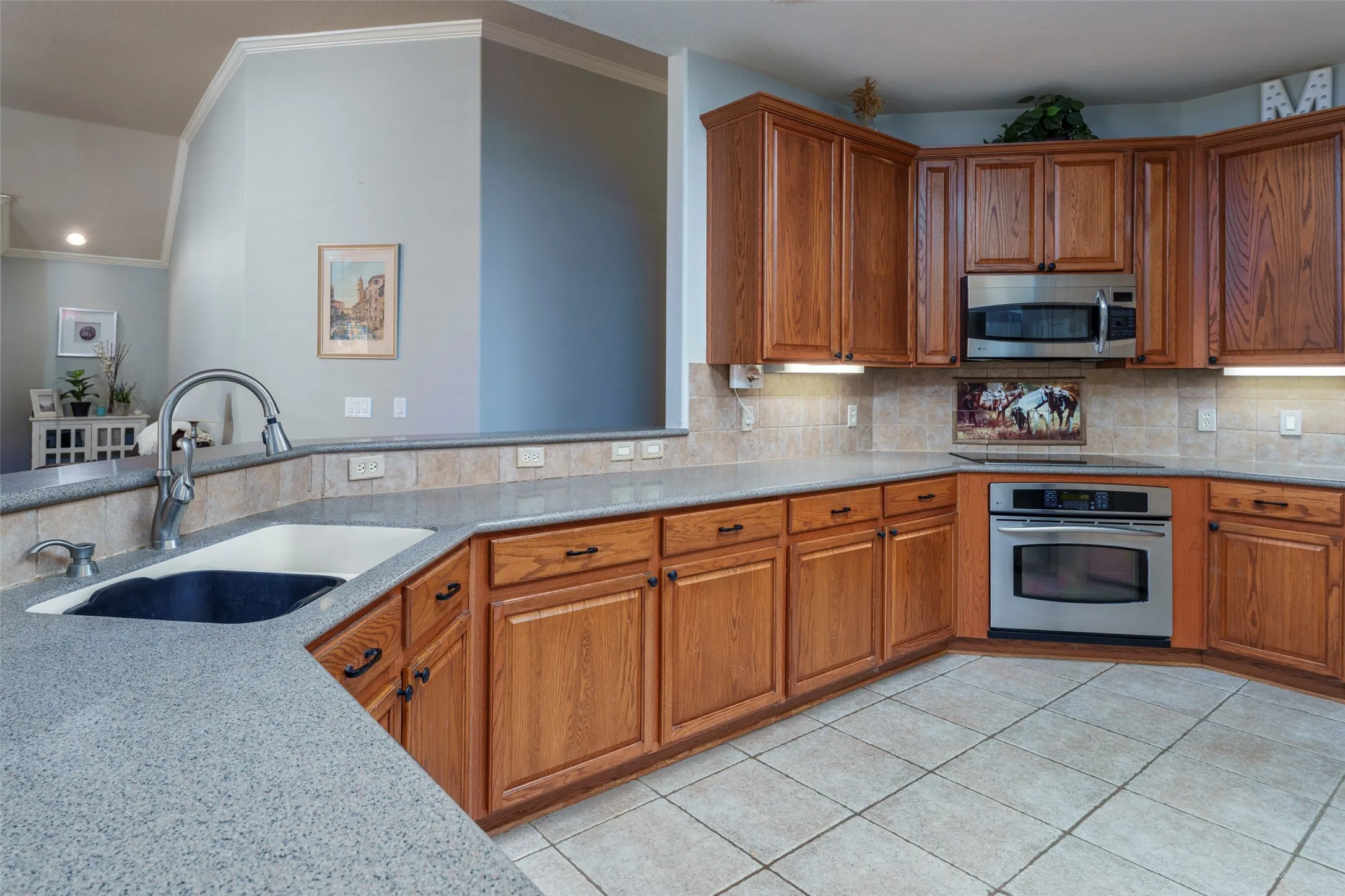 Kitchen featuring abundant wood cabinetry, integrated stainless steel appliances, speckled countertops, tile flooring, and a tile backsplash