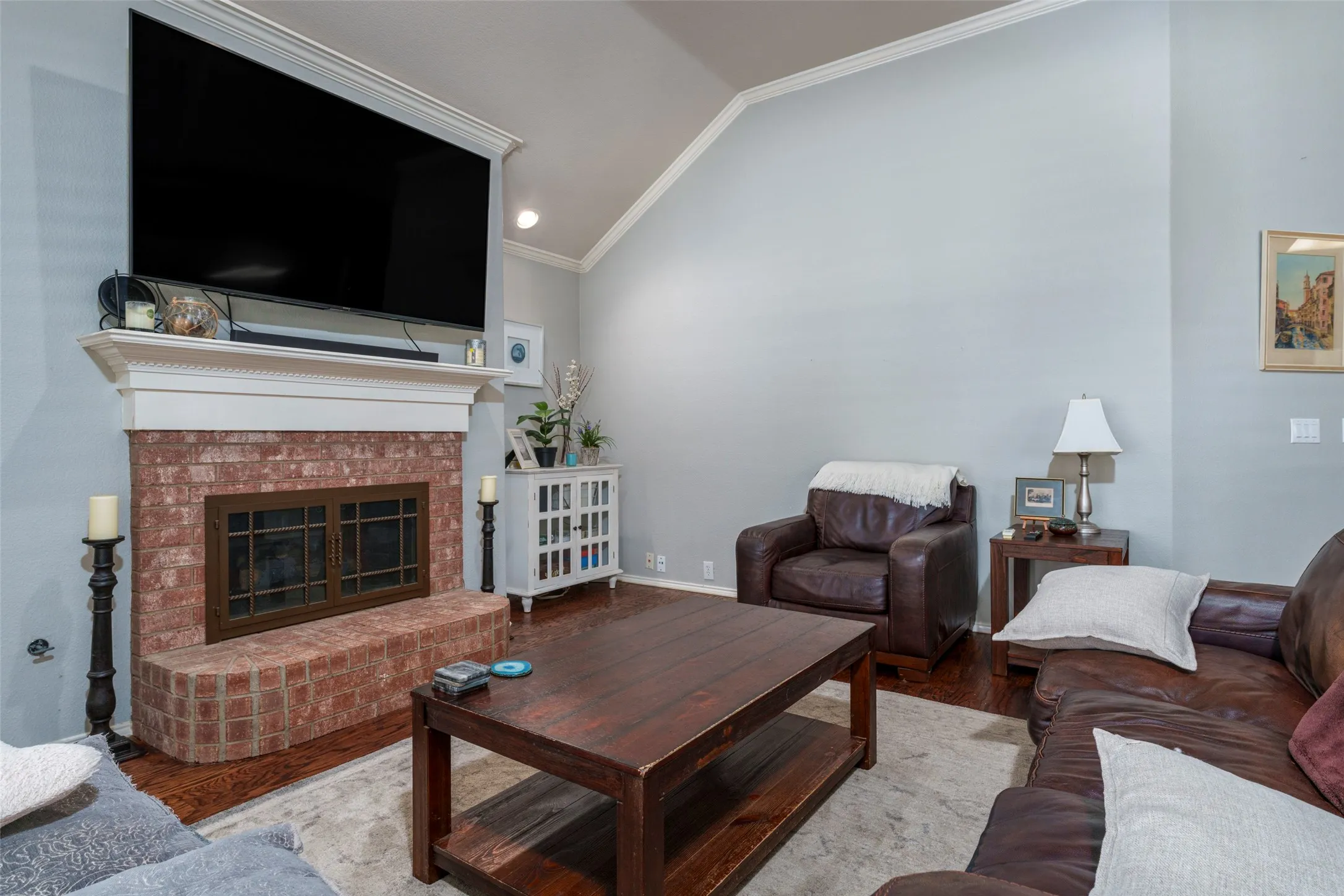 Brick fireplace with a substantial mantel, wood-finish flooring, and a vaulted ceiling