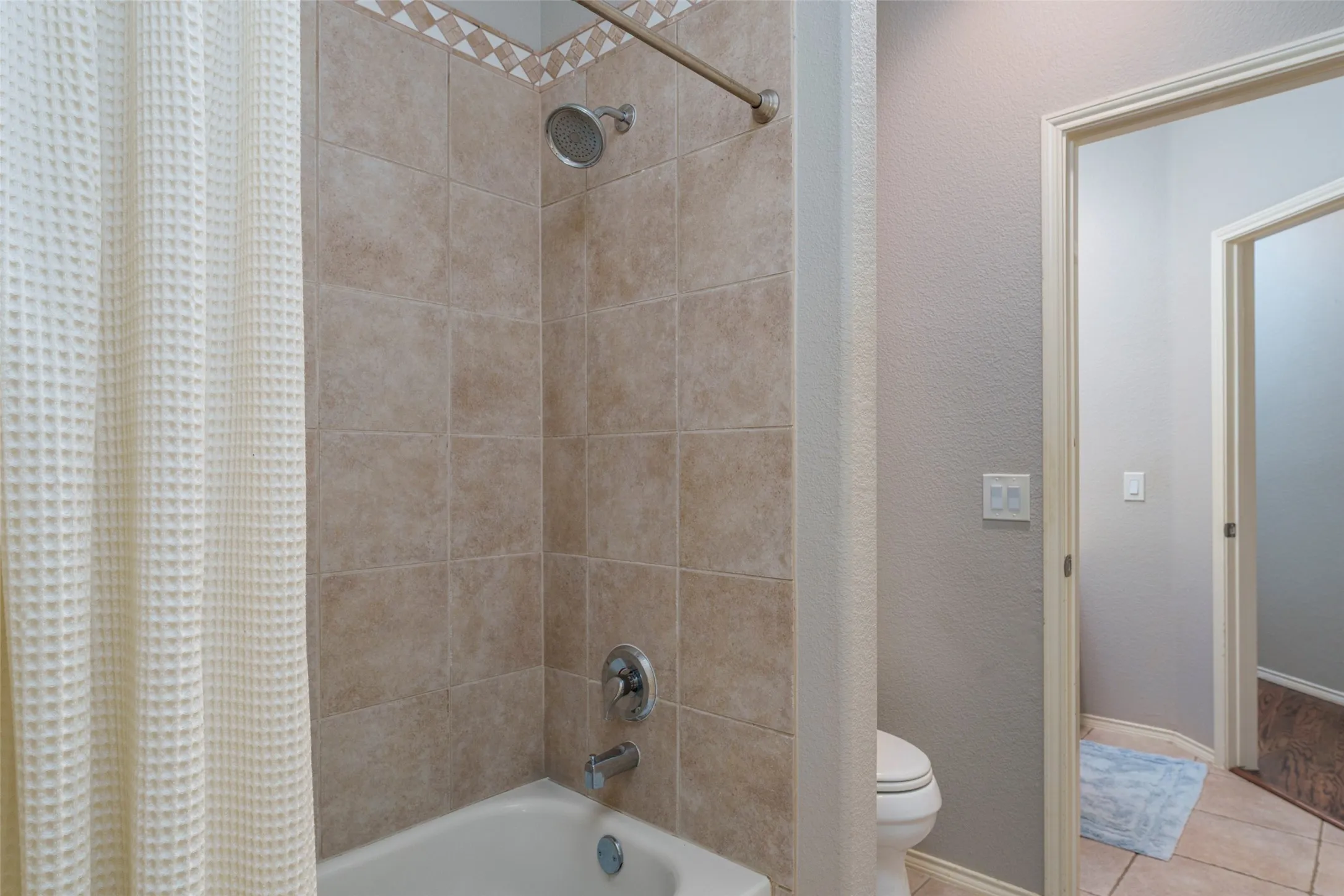 Bathtub with tiled surround, decorative tile accent, and brushed nickel fixtures
