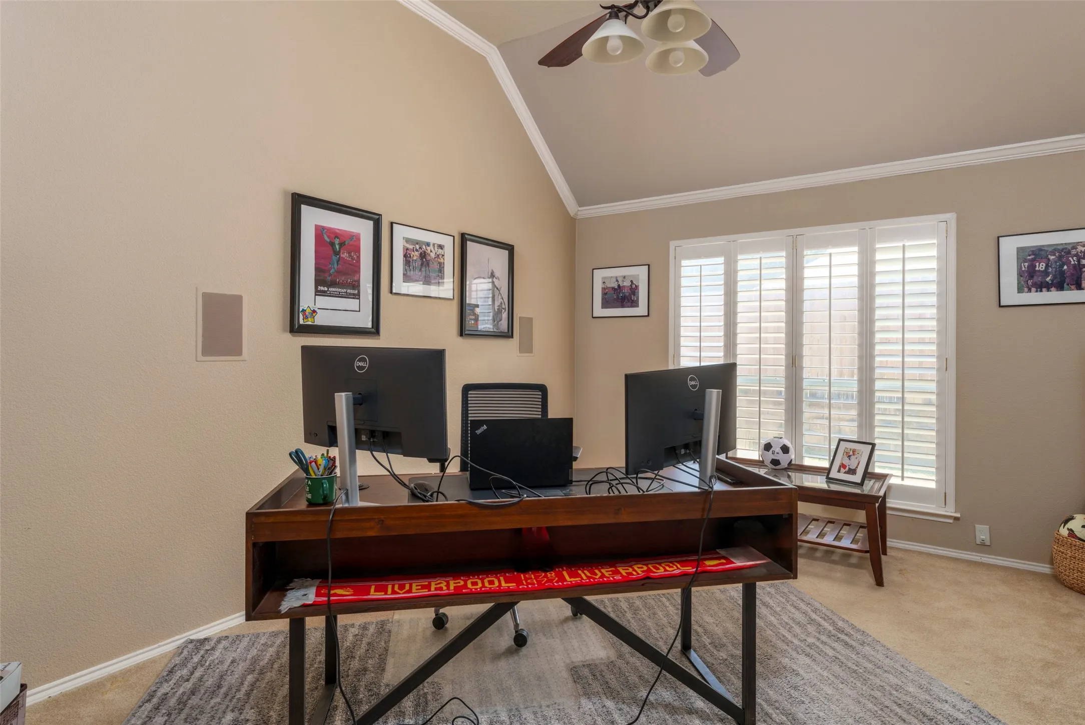 Vaulted ceiling with crown molding, ceiling fan with integrated lighting, built-in wall speakers, and plantation shutters on multiple windows