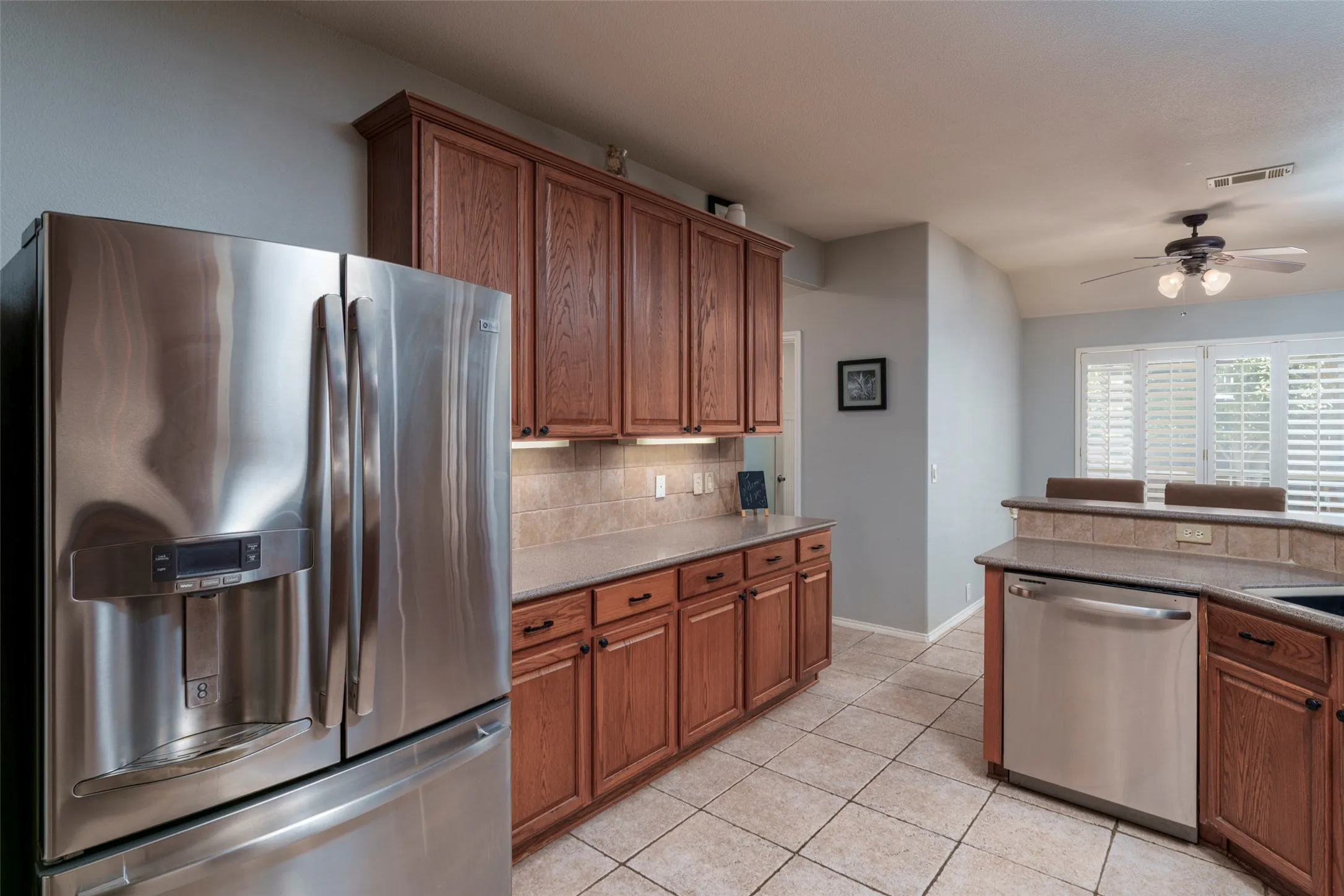 Kitchen featuring stainless steel appliances, wood cabinetry, tile flooring, and a ceiling fan