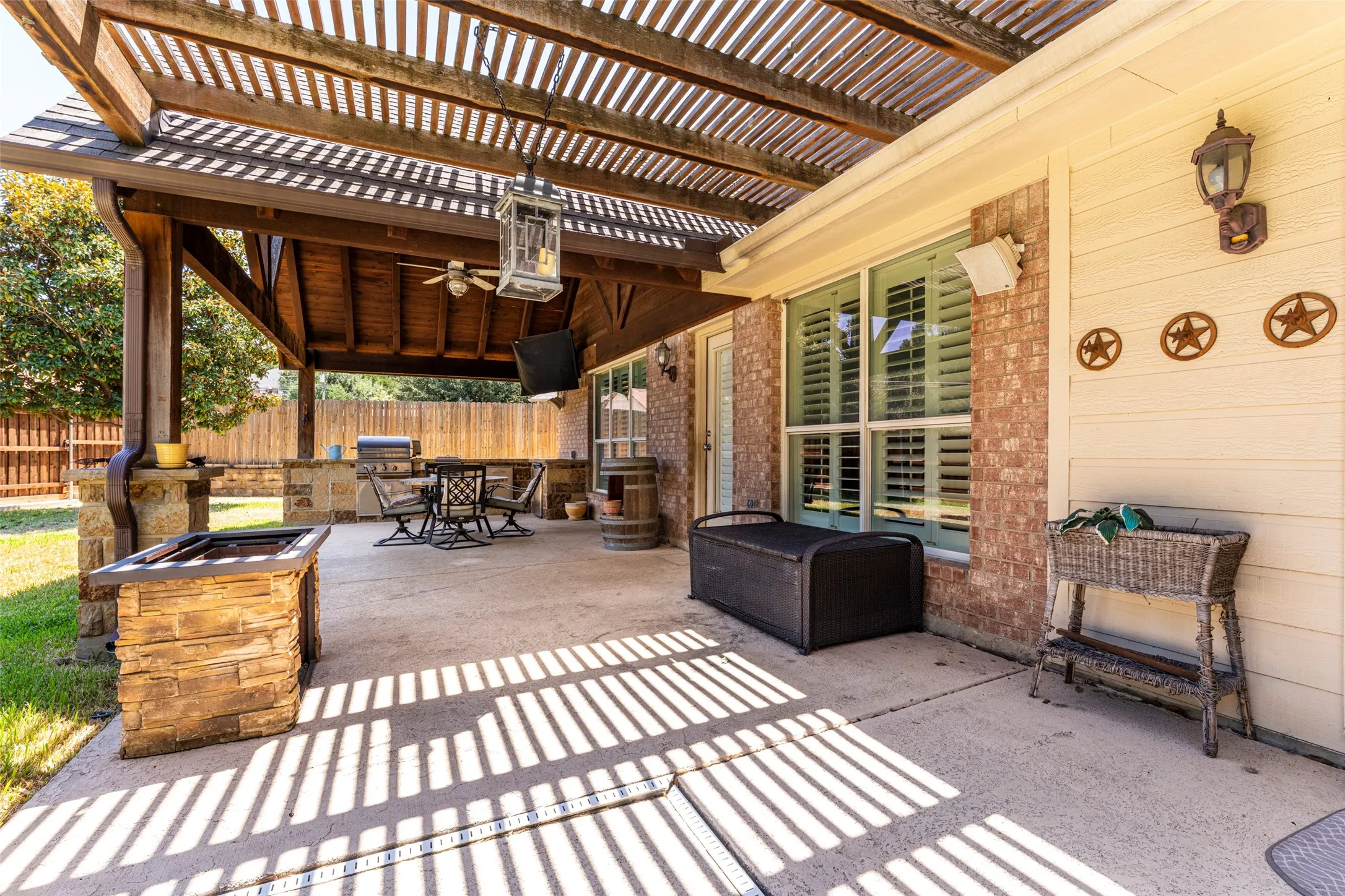 Expansive covered patio featuring a wood pergola, stone-clad outdoor kitchen, ceiling fan, and concrete flooring