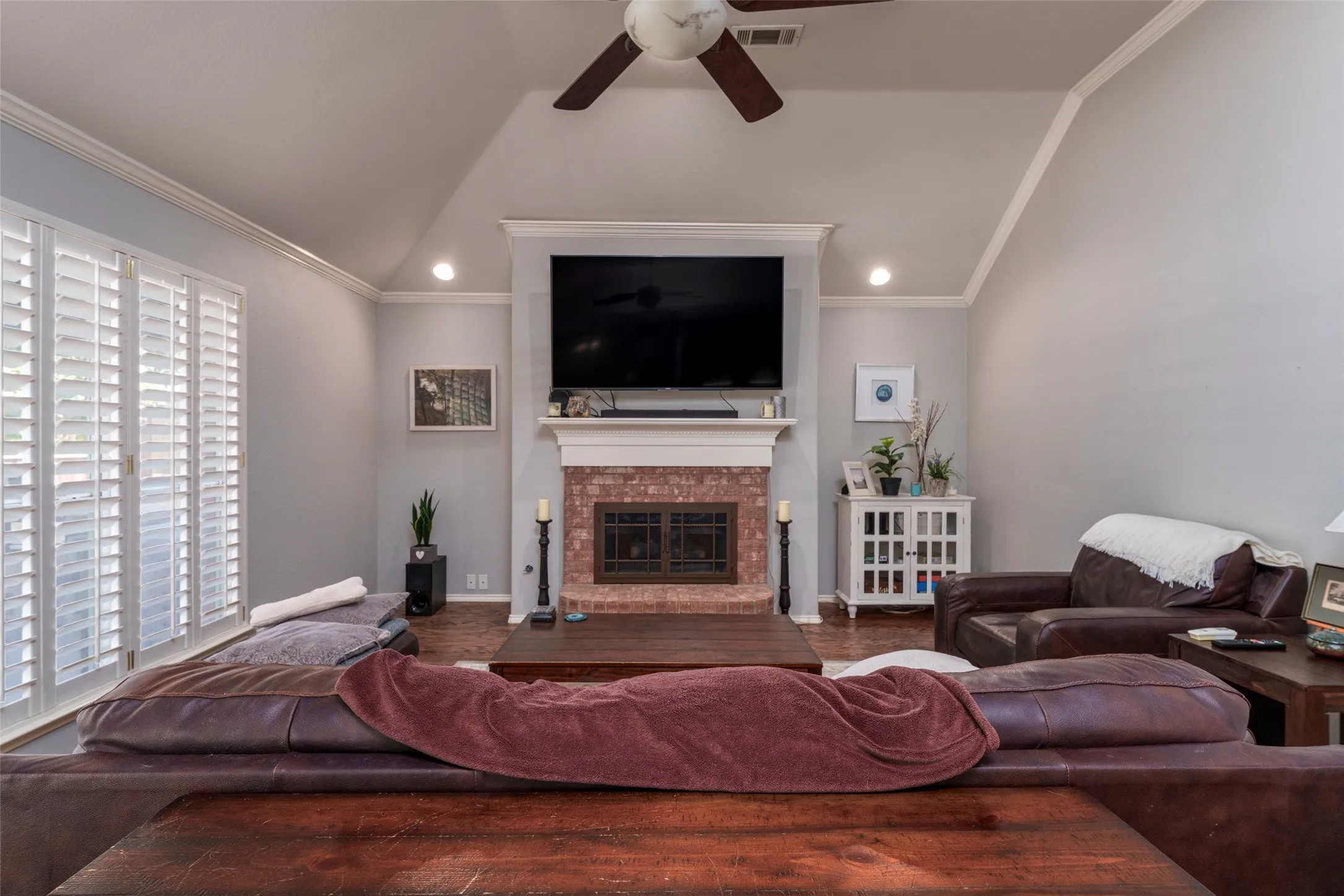 Living area featuring a brick fireplace with a white mantel, high vaulted ceilings, recessed lighting, and wood-finish flooring