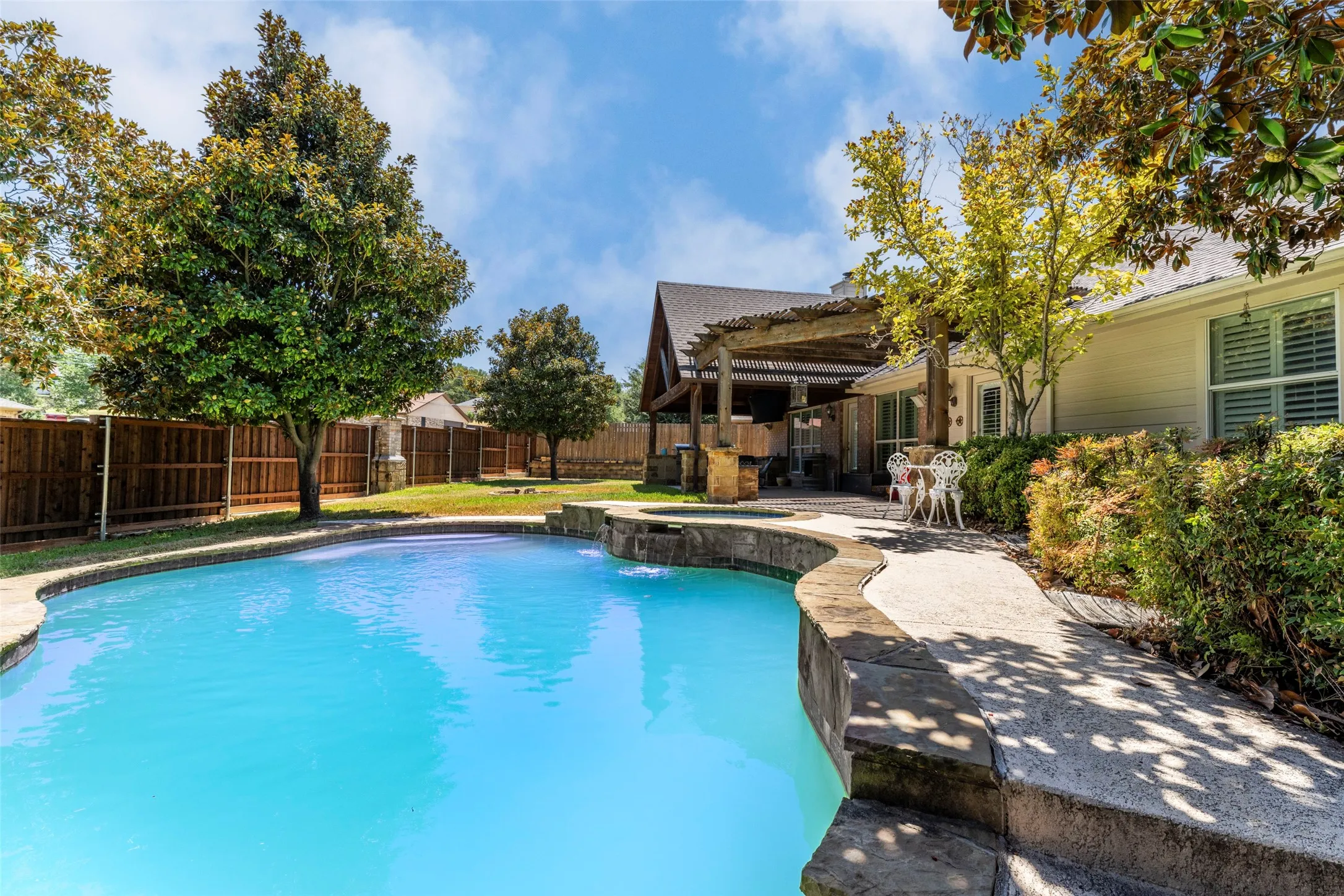 Curved swimming pool with stone coping, an integrated spa, and a water feature