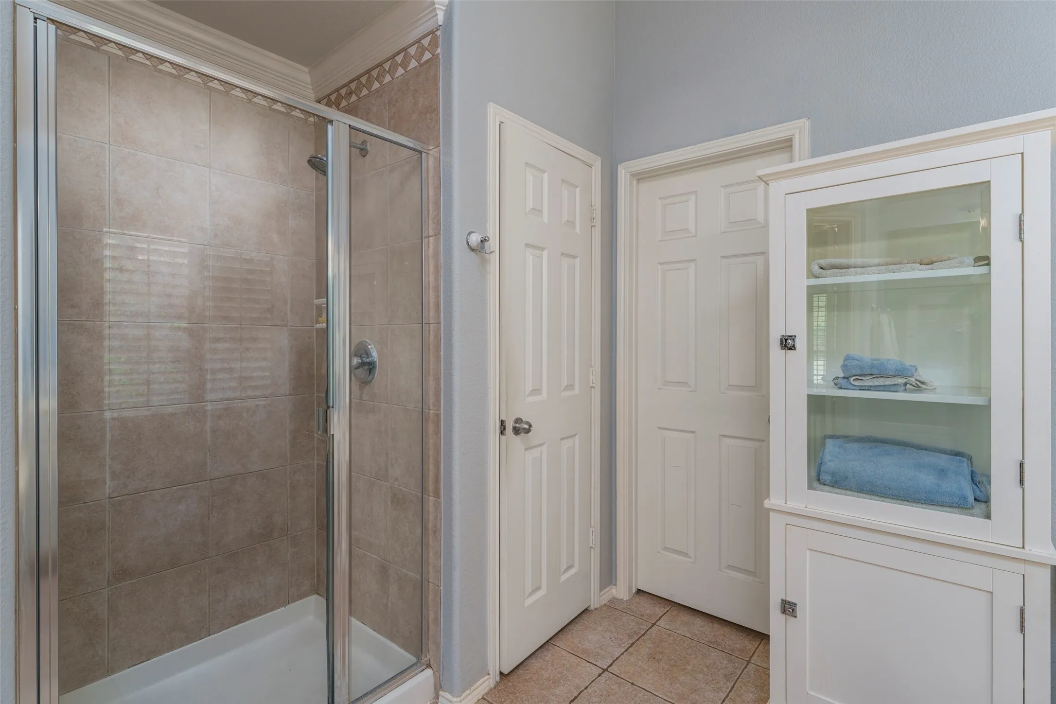 Glass-enclosed shower with tile surround, crown molding, and tiled flooring