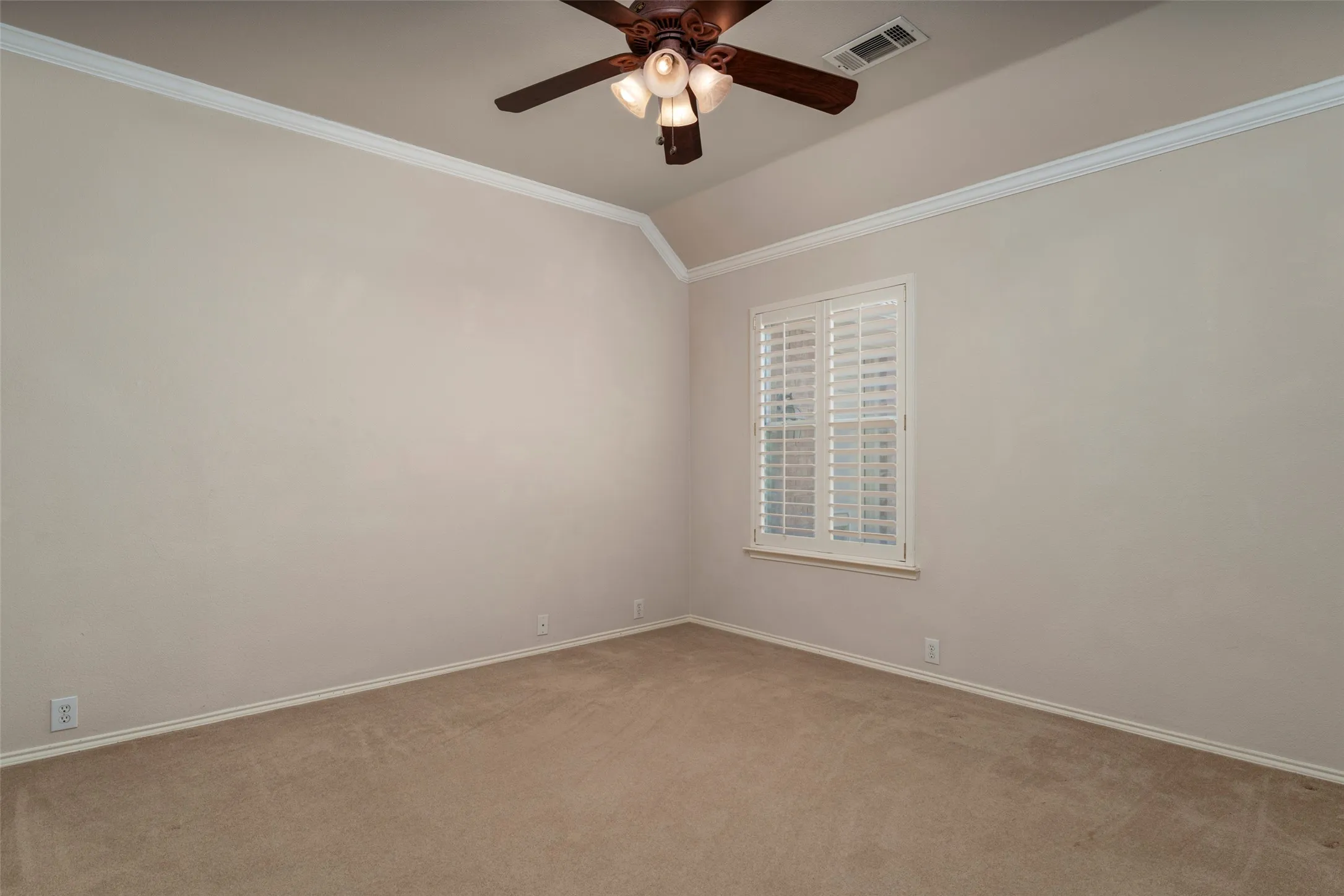 Vaulted ceiling with crown molding, ceiling fan, neutral carpet, and window with plantation shutters