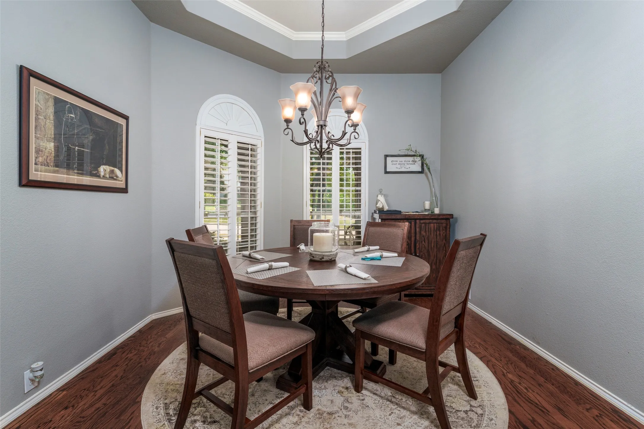 Tray ceiling, arched windows with plantation shutters, wood-finish flooring, and a decorative chandelier