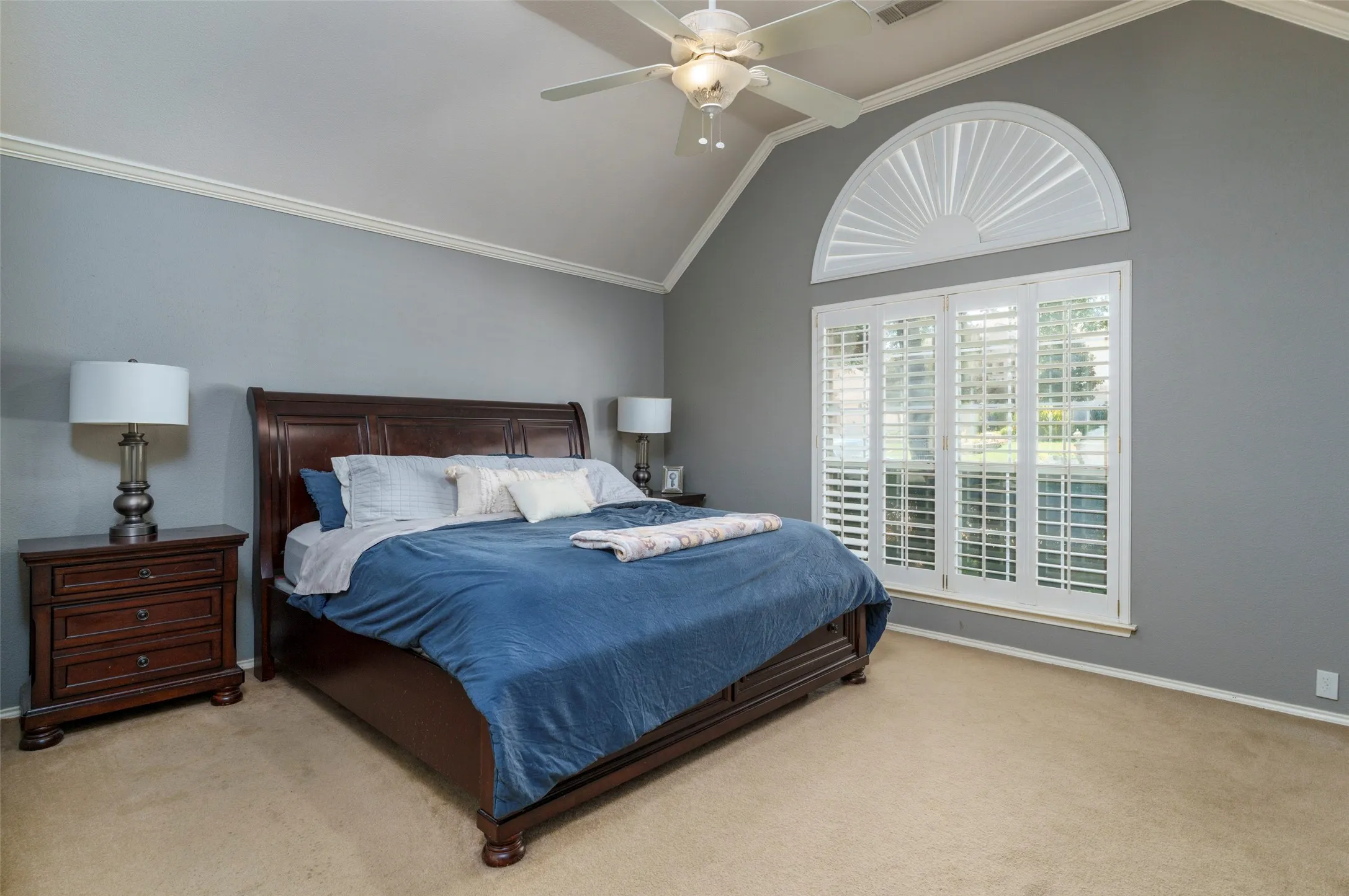 Vaulted ceiling with a ceiling fan, crown molding, arched transom window, and plantation shutters