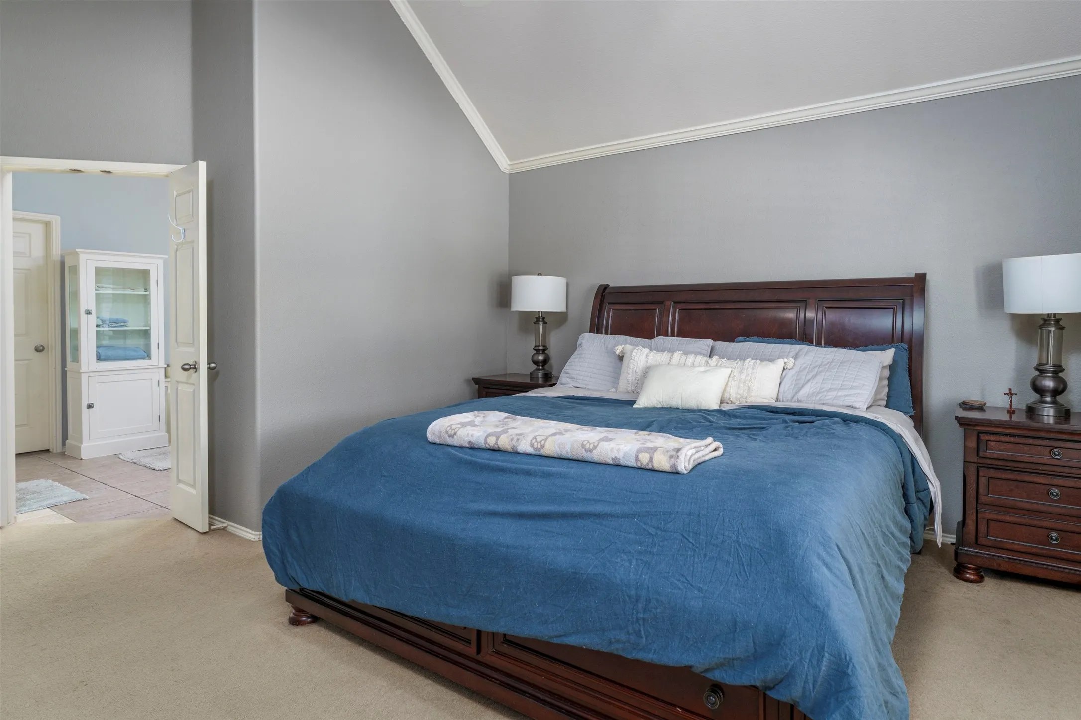 Vaulted ceiling with crown molding, carpeted flooring, and a white built-in display cabinet