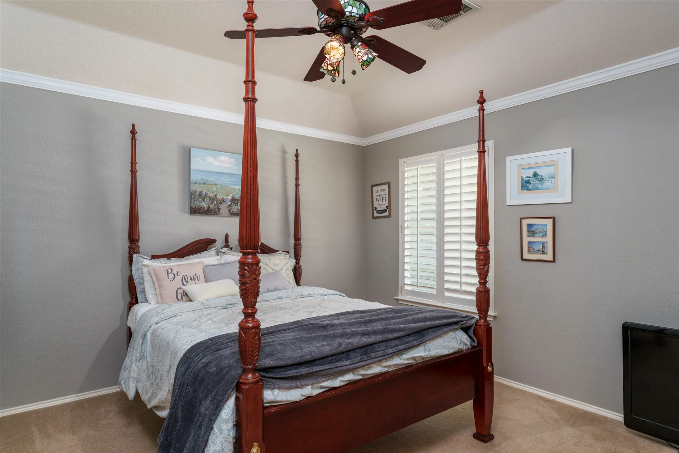 Vaulted ceiling with decorative fan, crown molding, plantation shutters, and carpeted flooring