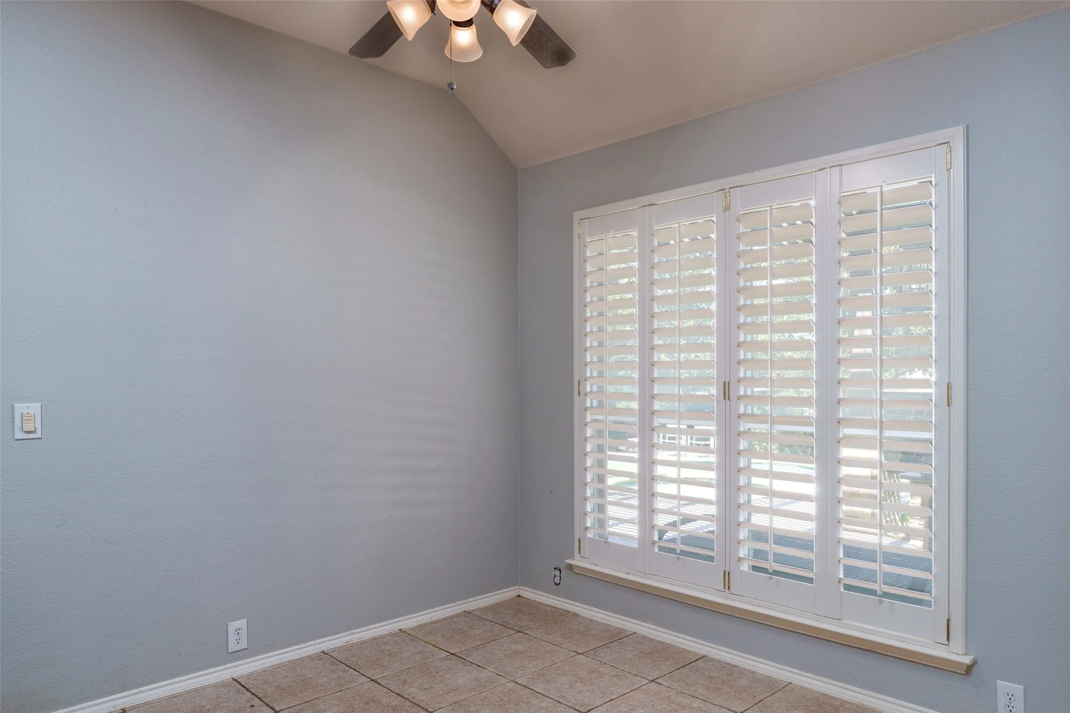 Vaulted ceiling with a ceiling fan, white plantation shutters, and light-toned flooring