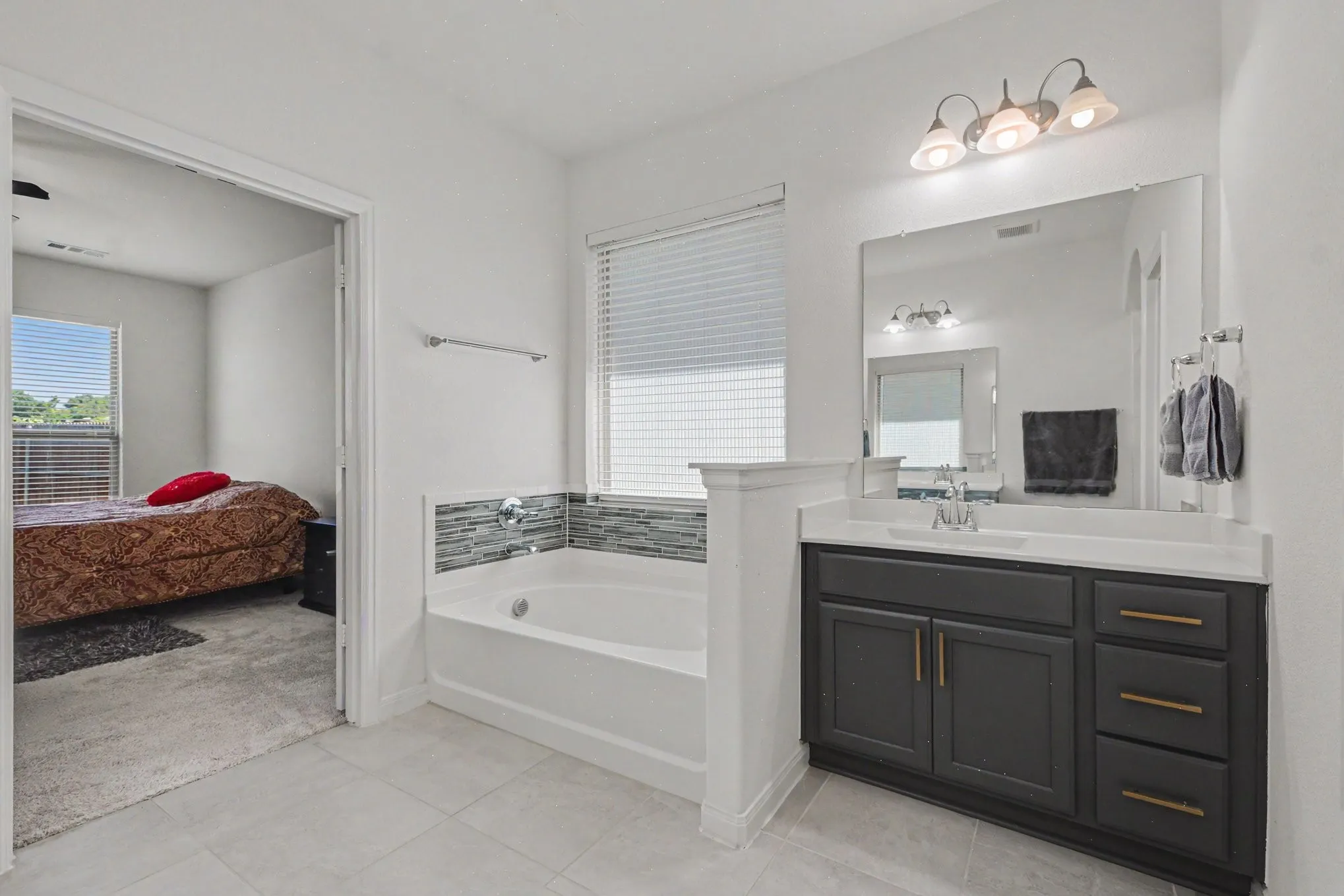 Bathroom featuring a built-in bathtub, mosaic tile accent, single vanity with dark cabinetry, integrated sink, and wall-mounted mirror