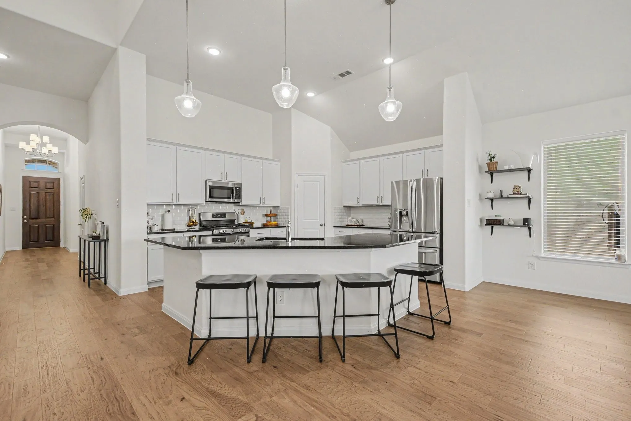Kitchen featuring white cabinetry, black countertops, stainless steel appliances, and a central island with pendant lighting