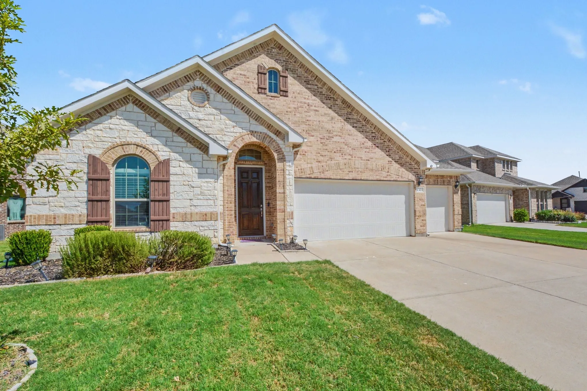 Stone and brick exterior with arched entryways, a two-car garage, and a concrete driveway