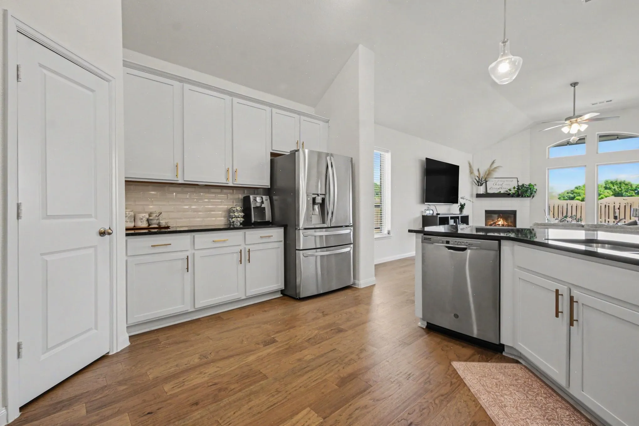 Kitchen featuring wood-finish flooring, white cabinetry, dark countertops, a tile backsplash, and stainless steel appliances