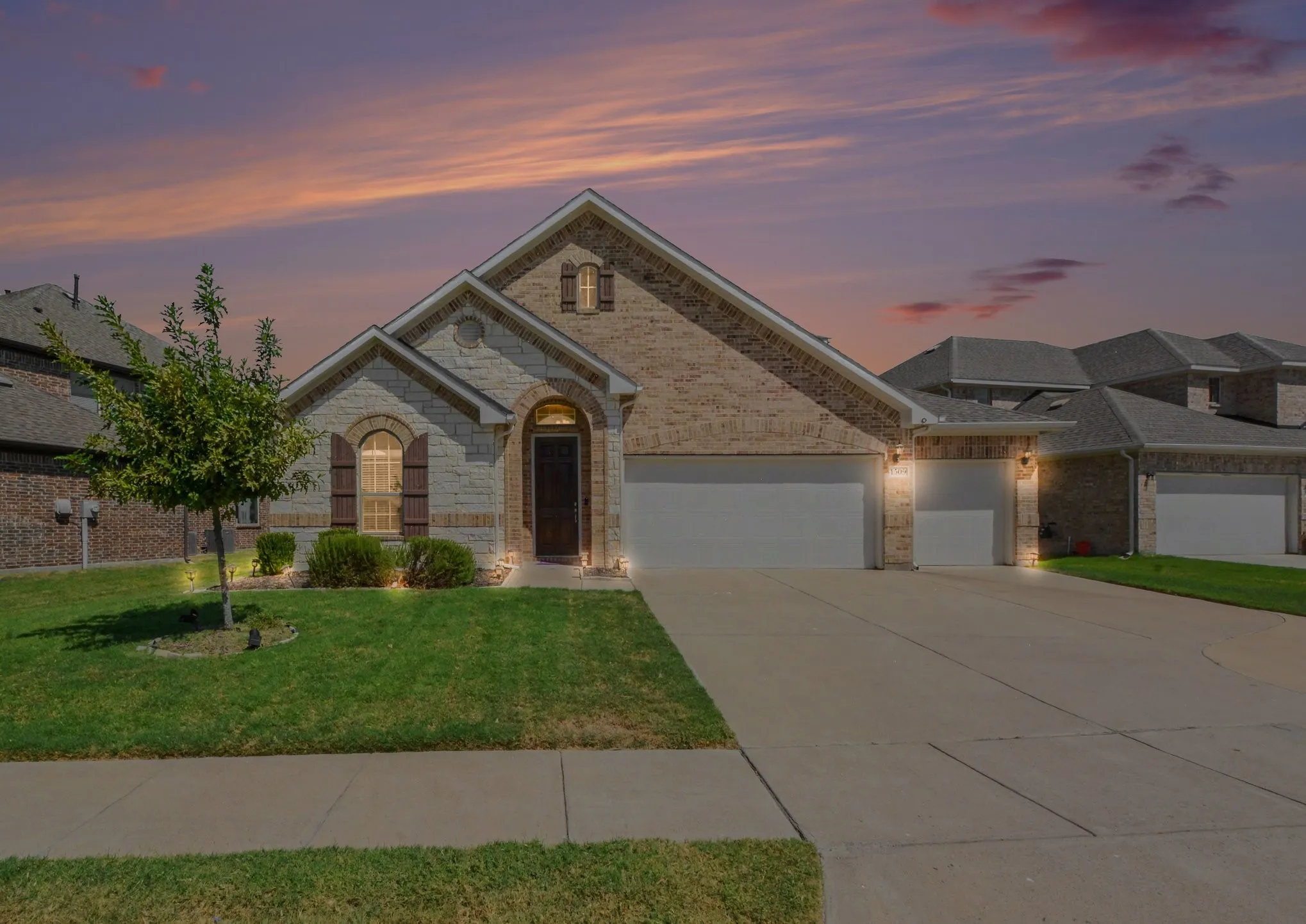 Brick and stone facade with arched entry, dual garage doors, and front yard landscaping