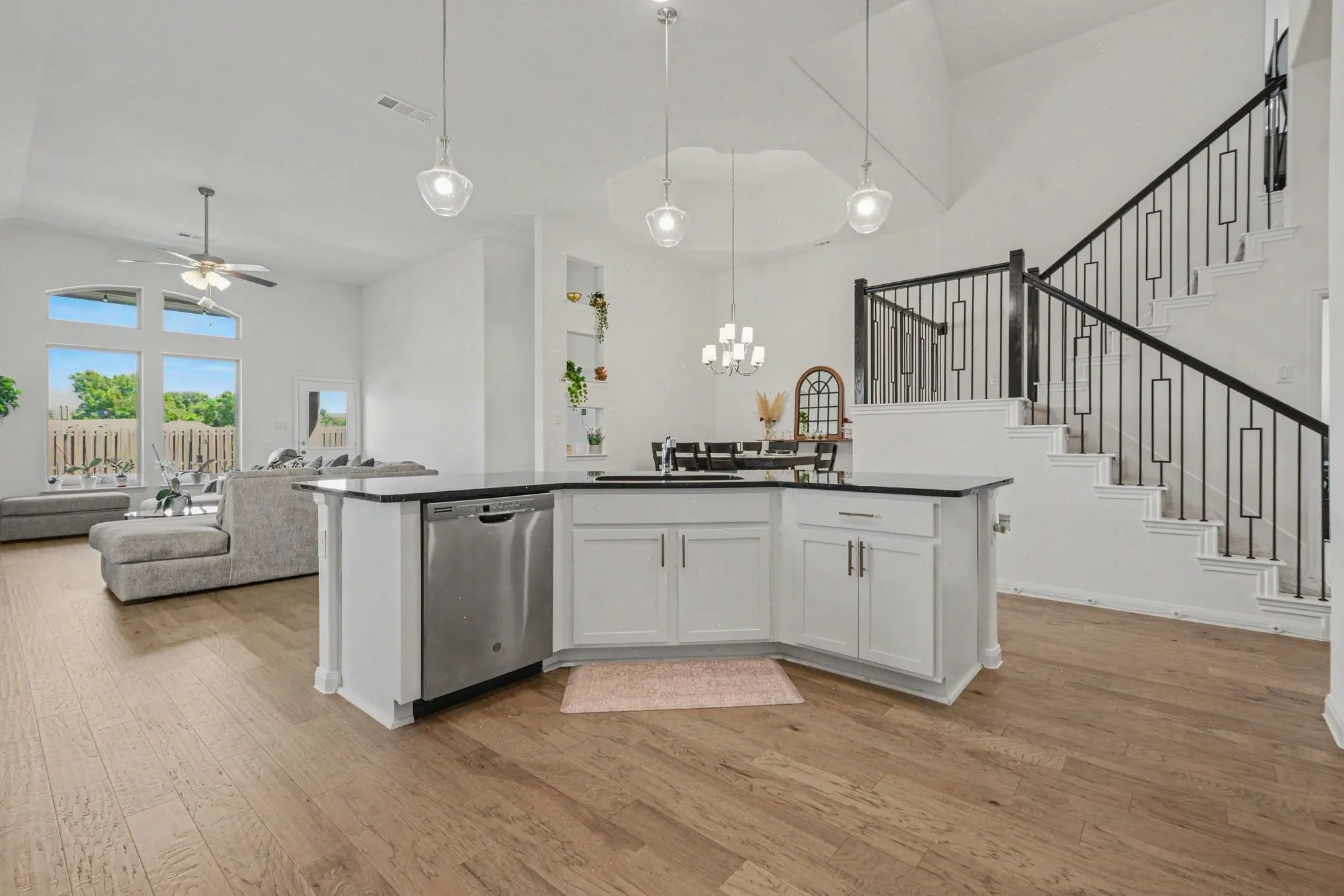 Open concept living space with wood-finish flooring, a kitchen island with built-in stainless steel dishwasher, and a staircase featuring wrought iron balusters
