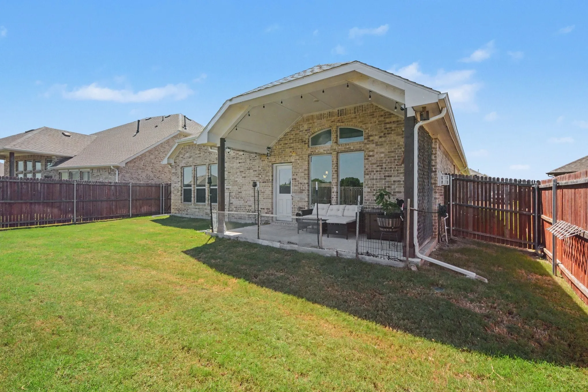 Expansive backyard with a manicured lawn, brick exterior, covered patio, and privacy fencing