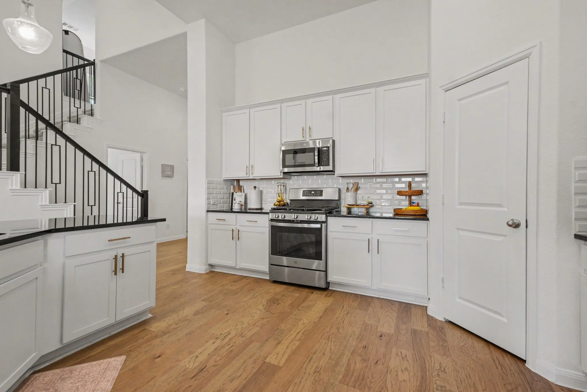 Kitchen featuring white shaker cabinetry, stainless steel appliances, dark countertops, a subway tile backsplash, and wood-finish flooring