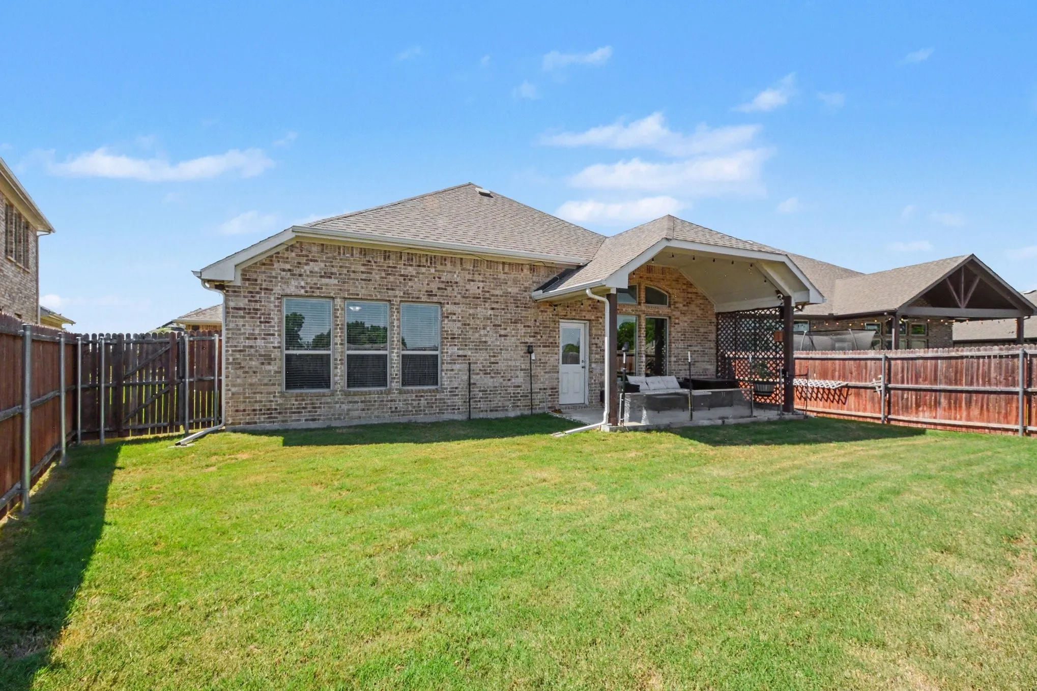 Expansive backyard with a covered patio, brick exterior, wood privacy fence, and a separate covered structure