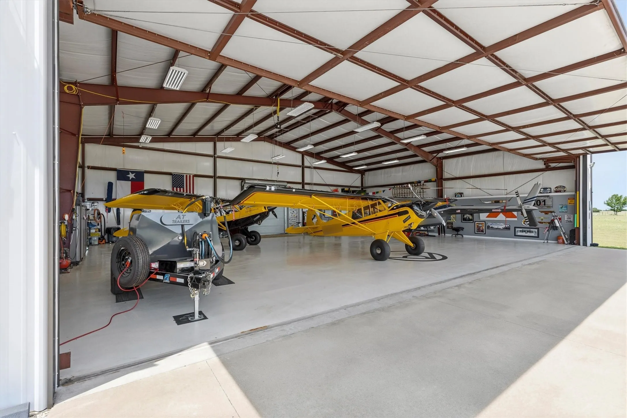 Spacious hangar with a high-clearance bi-fold door, exposed structural beams, polished concrete flooring, and ceiling-mounted fluorescent lighting