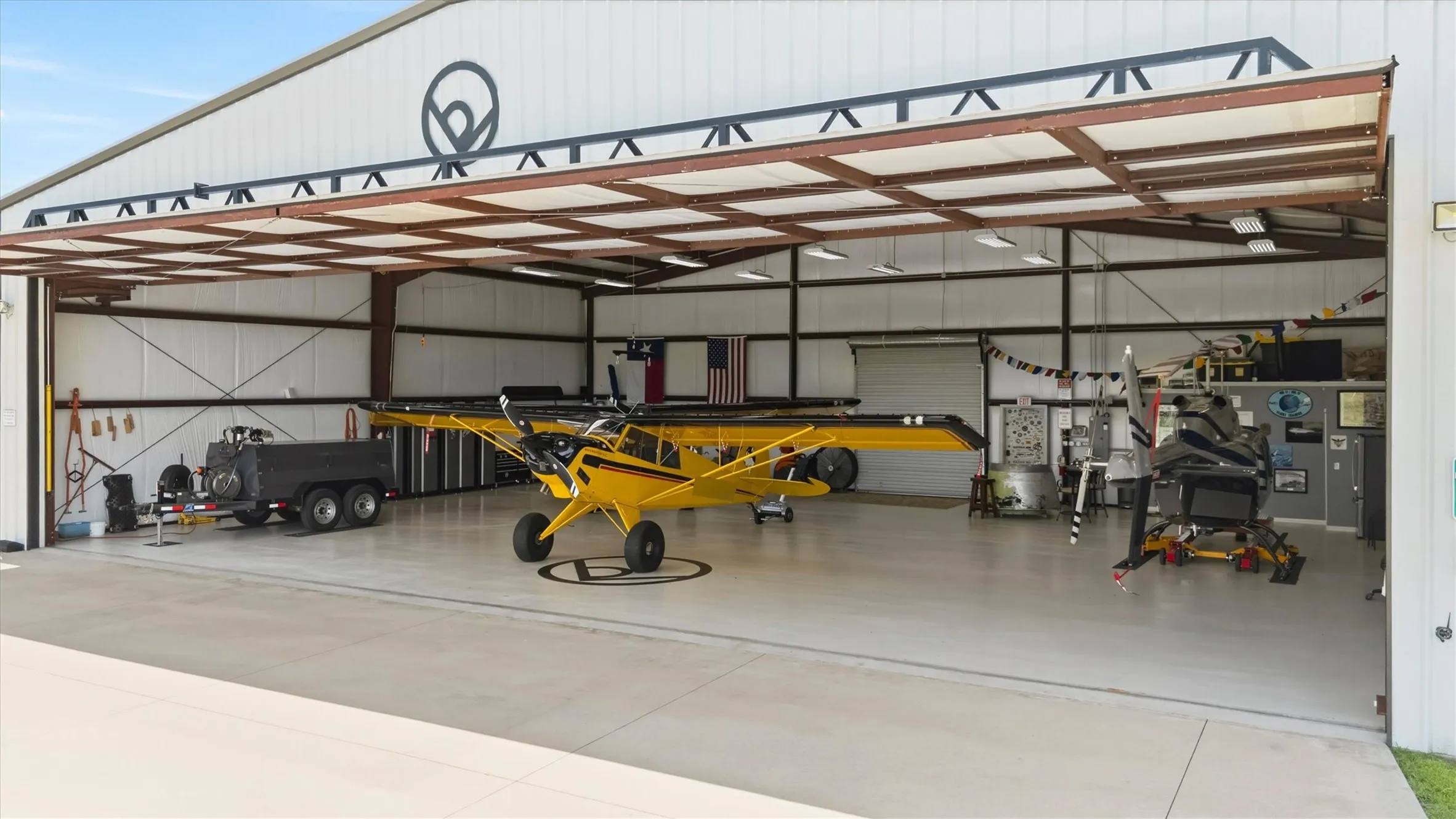 Expansive hangar featuring a large bi-fold door, polished concrete flooring, exposed steel framing, and bright overhead lighting