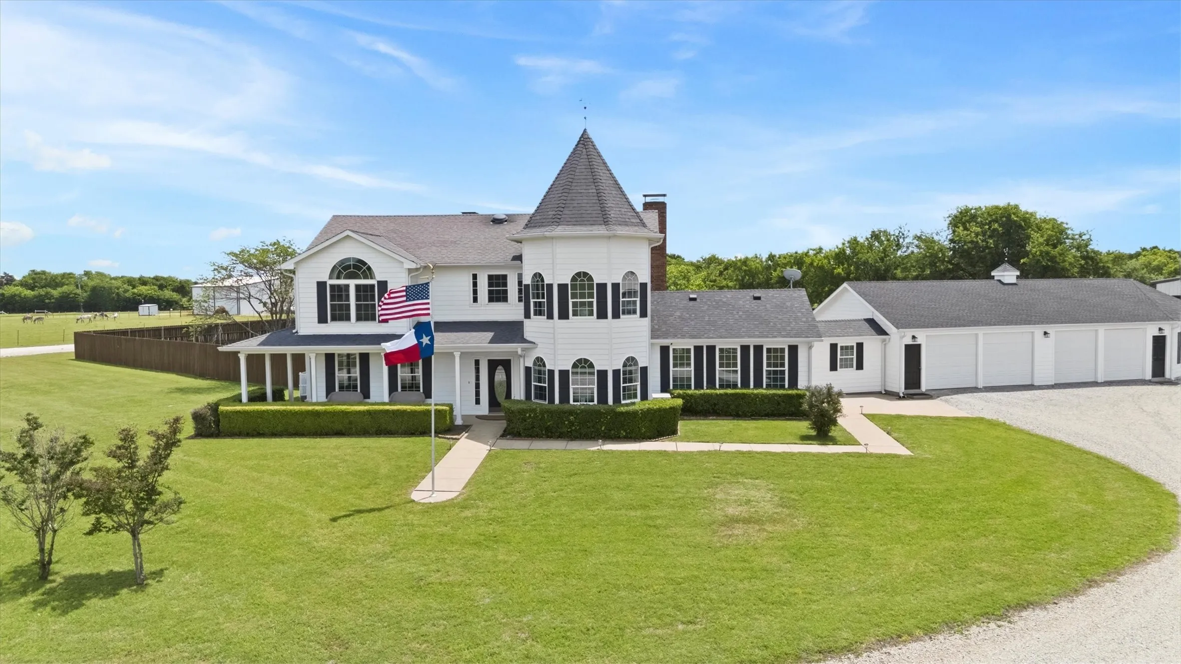White exterior with a turret, multiple dormer windows, covered front porch, and a gravel driveway