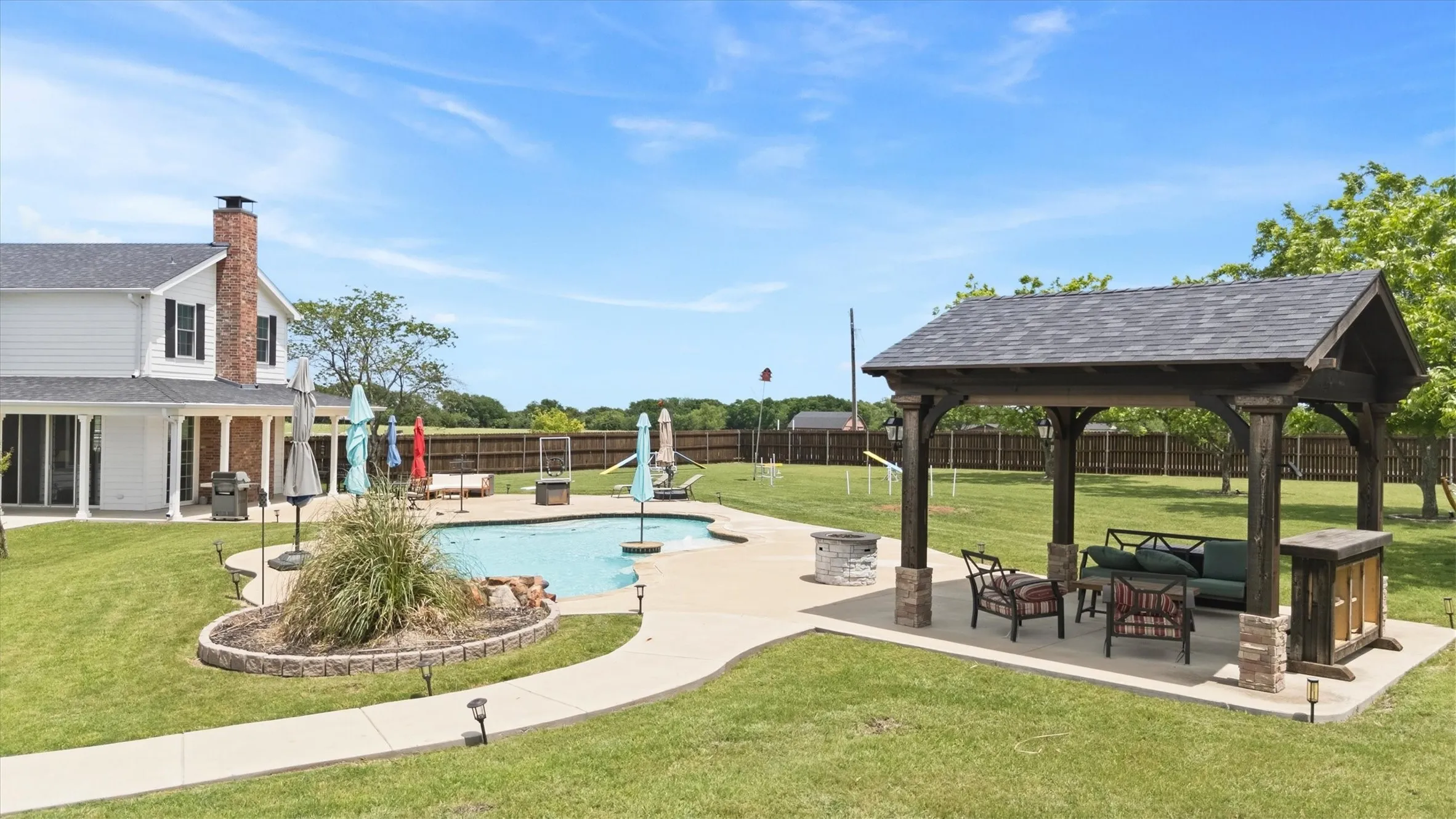 Expansive backyard featuring an in-ground swimming pool, a dedicated patio area, and a large wooden gazebo with a shingled roof