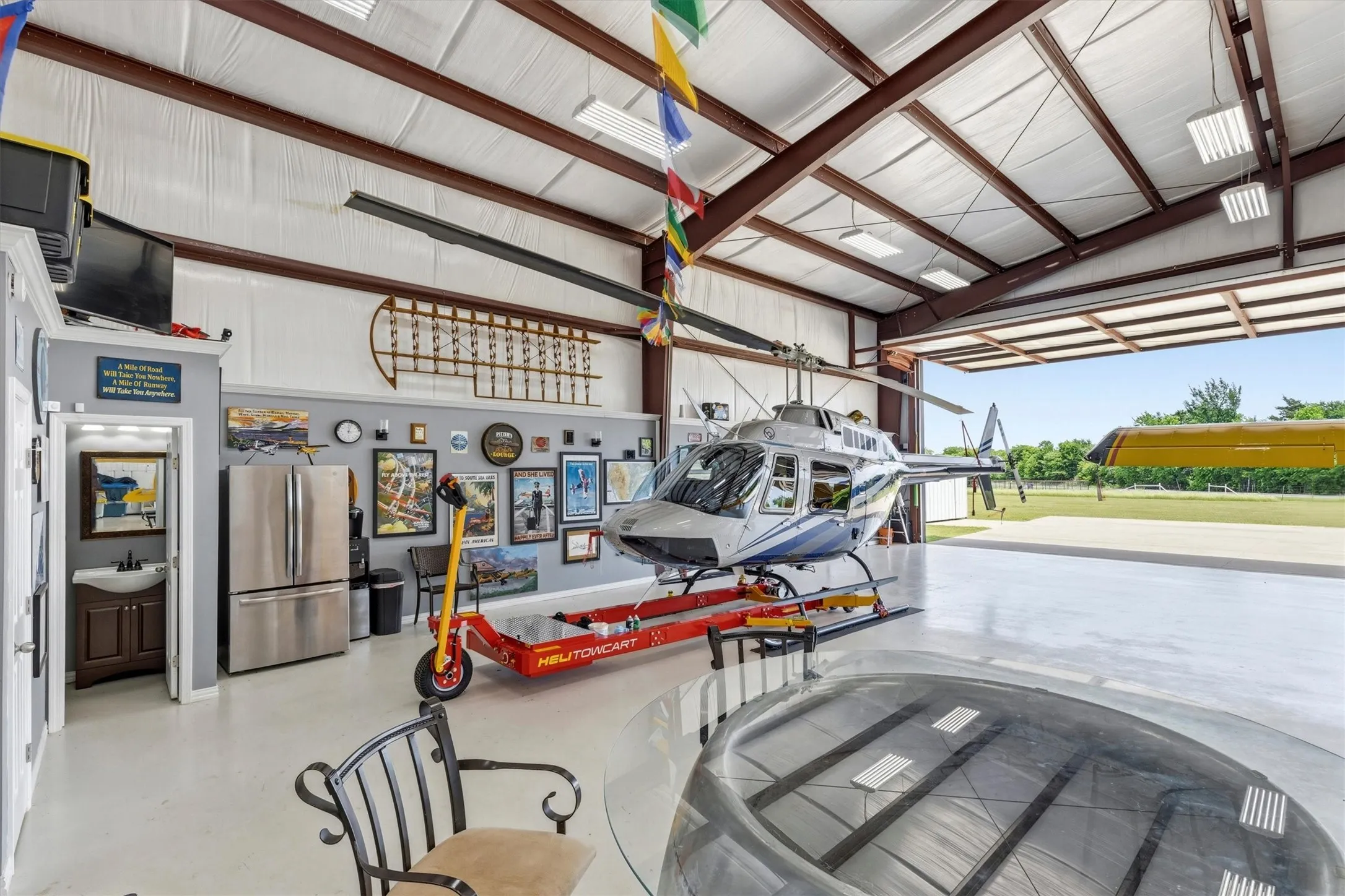 Spacious hangar featuring an expansive concrete floor, exposed beam ceiling, bright overhead lighting, and a large roll-up door